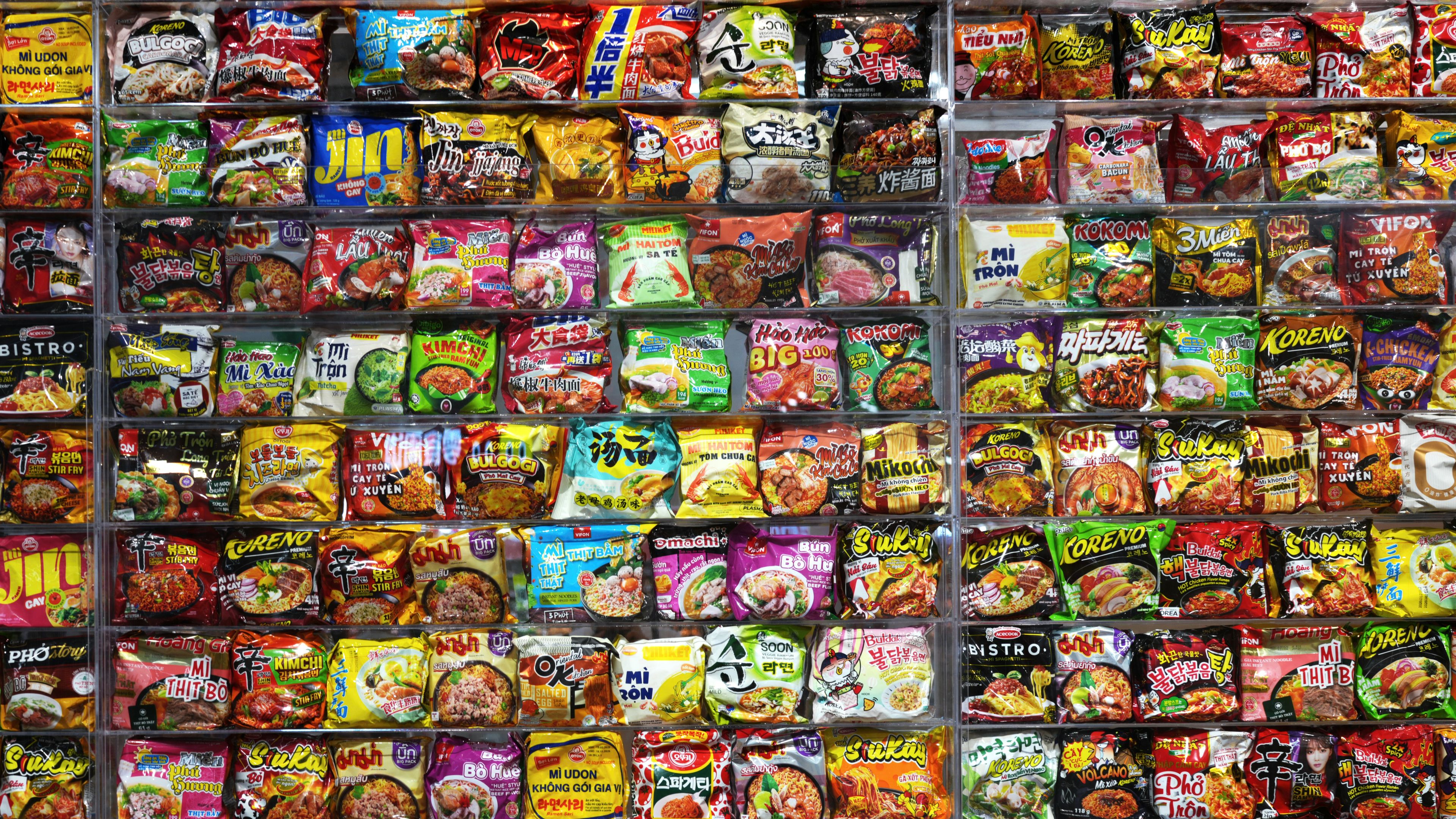 A large display of colorful instant noodle packages arranged on shelves in a store