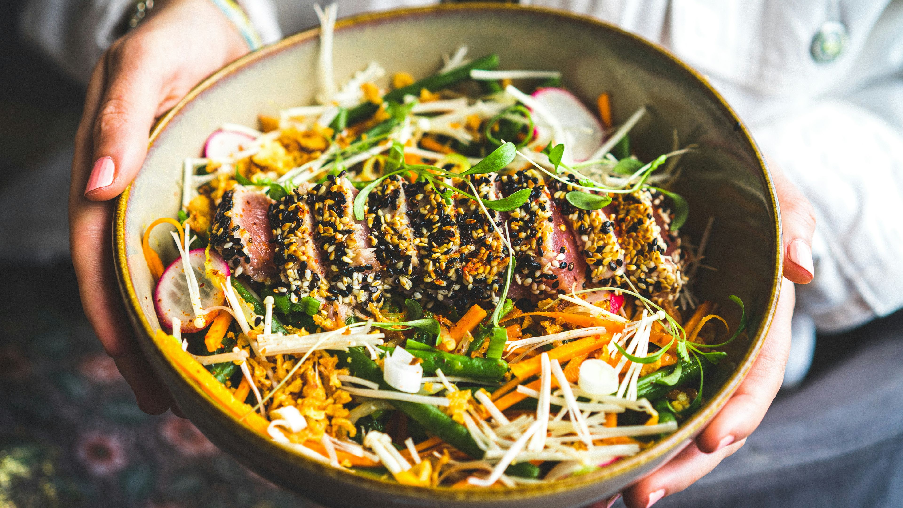 Person holding black ceramic bowl with vegetable salad