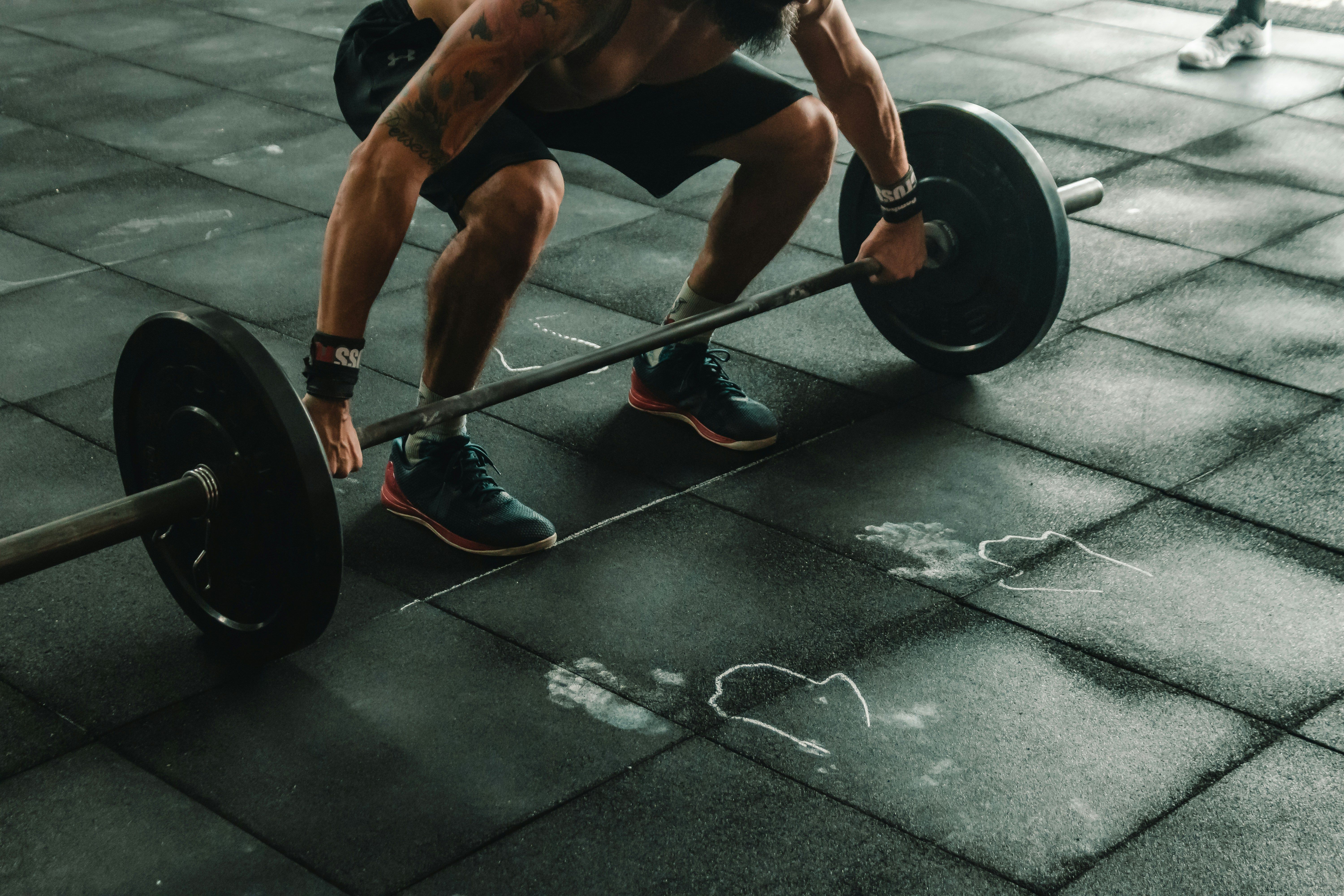 A person lifting a heavy barbell from a black rubber gym floor