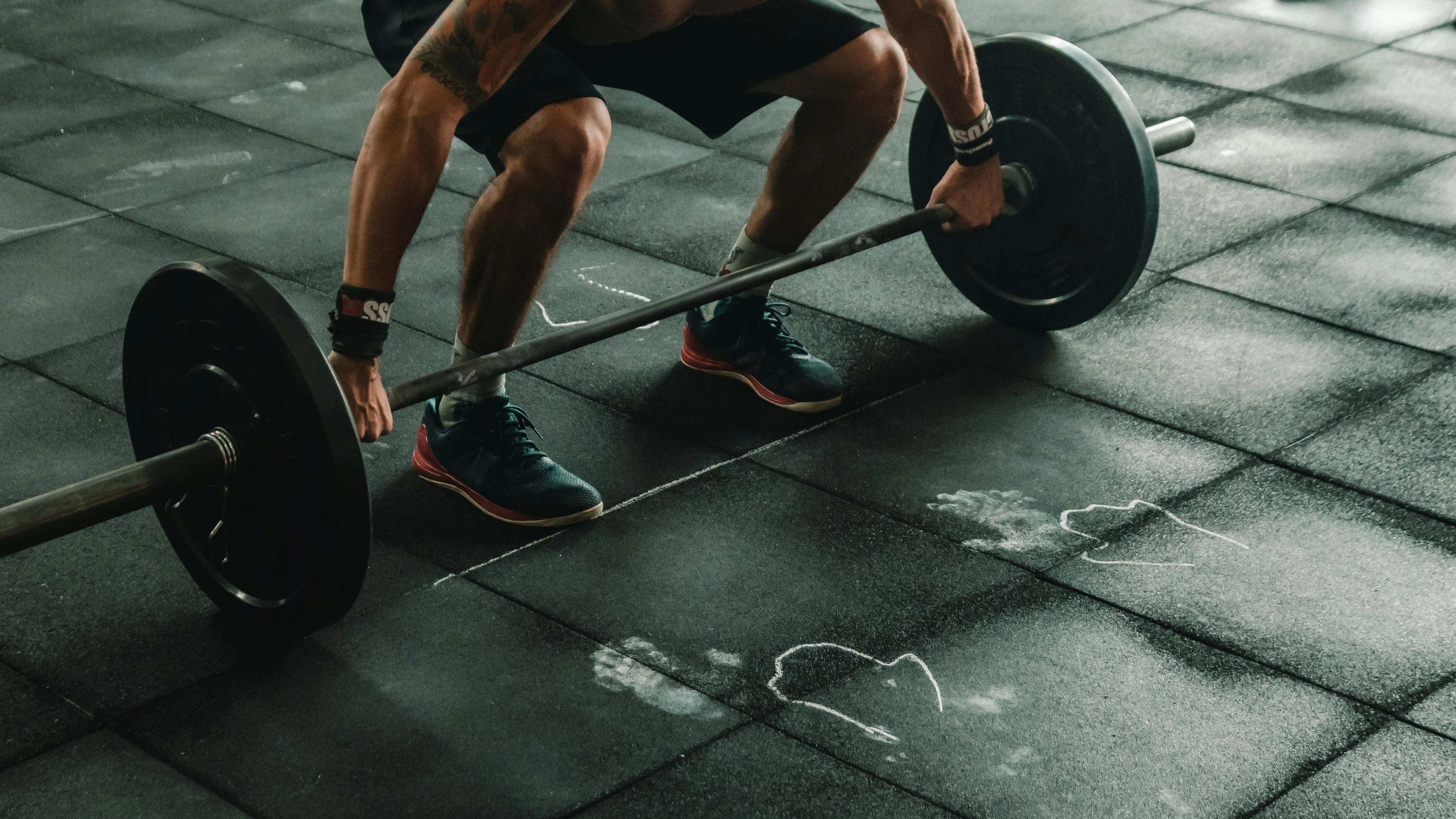 A person lifting a heavy barbell from a black rubber gym floor