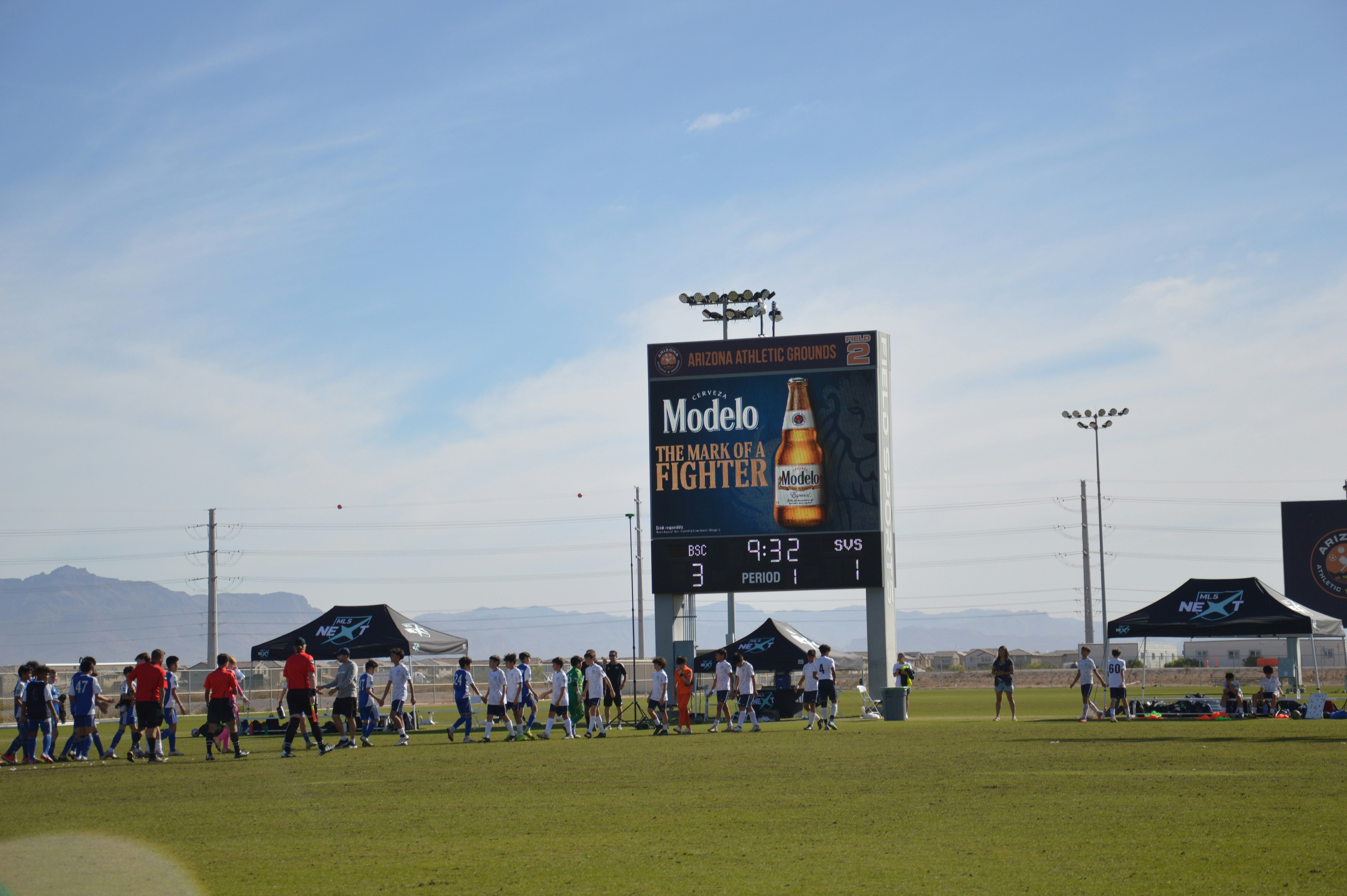 People gather on a sports field near a large scoreboard