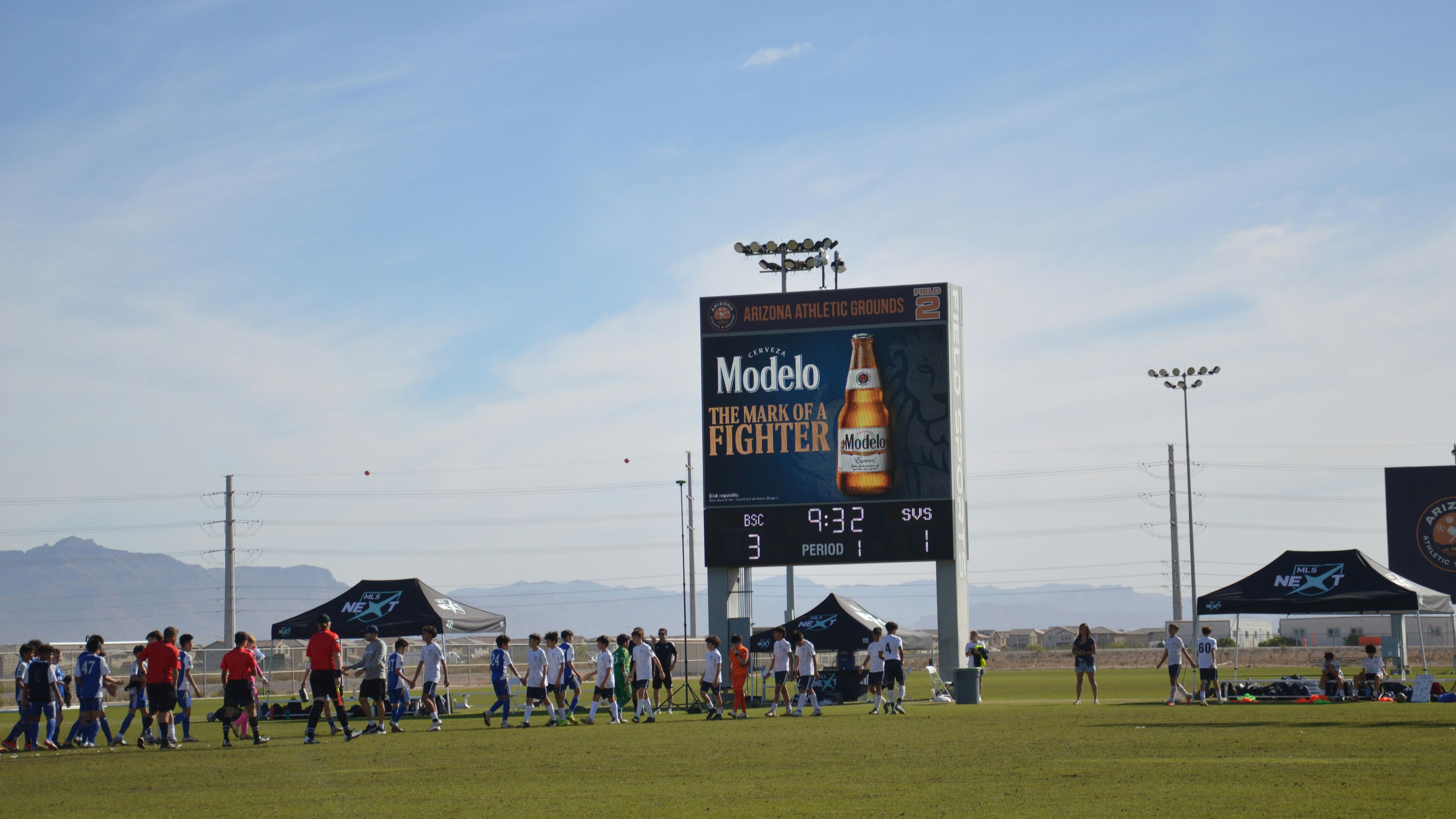 People gather on a sports field near a large scoreboard