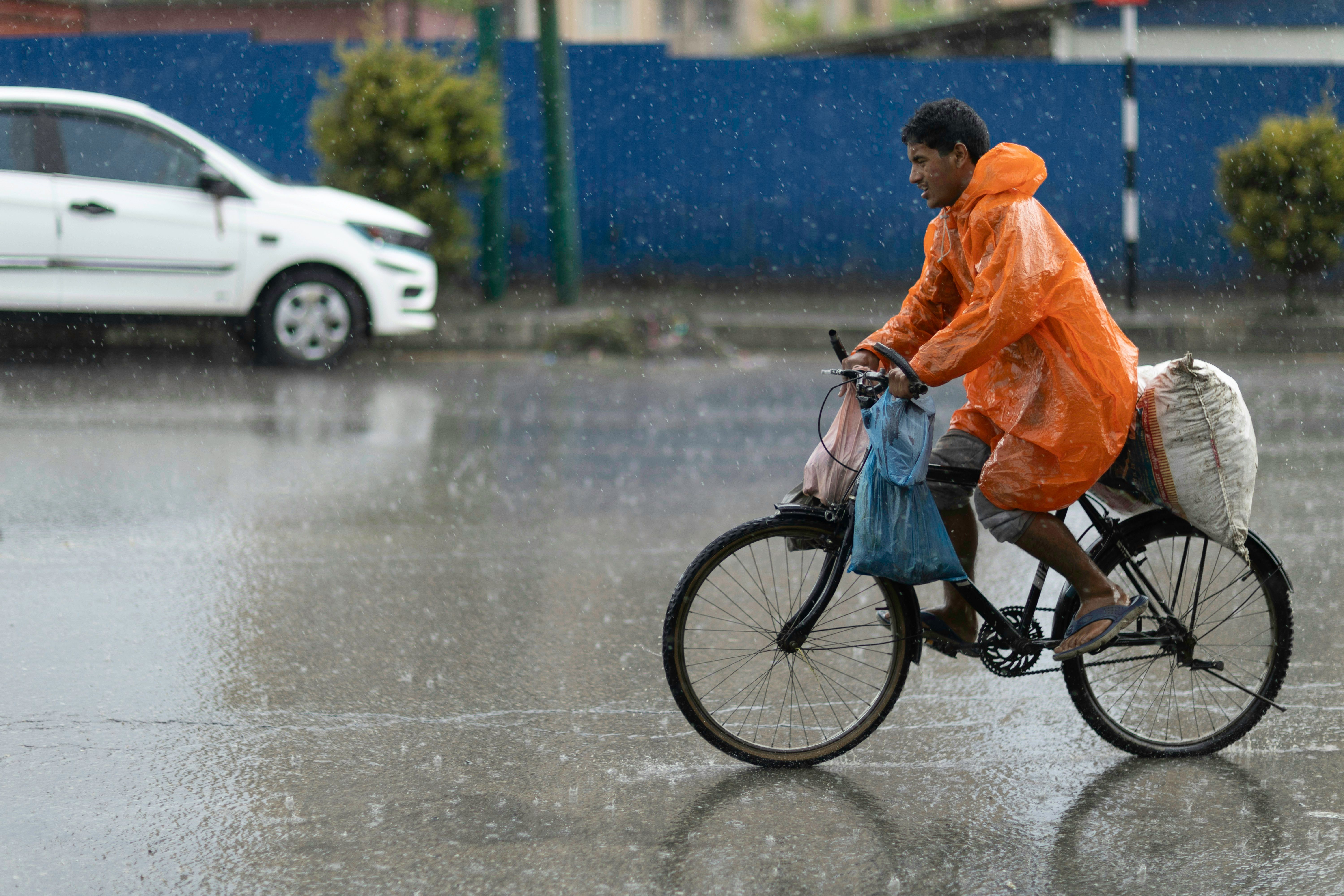 Man in orange raincoat rides bicycle through heavy rain.