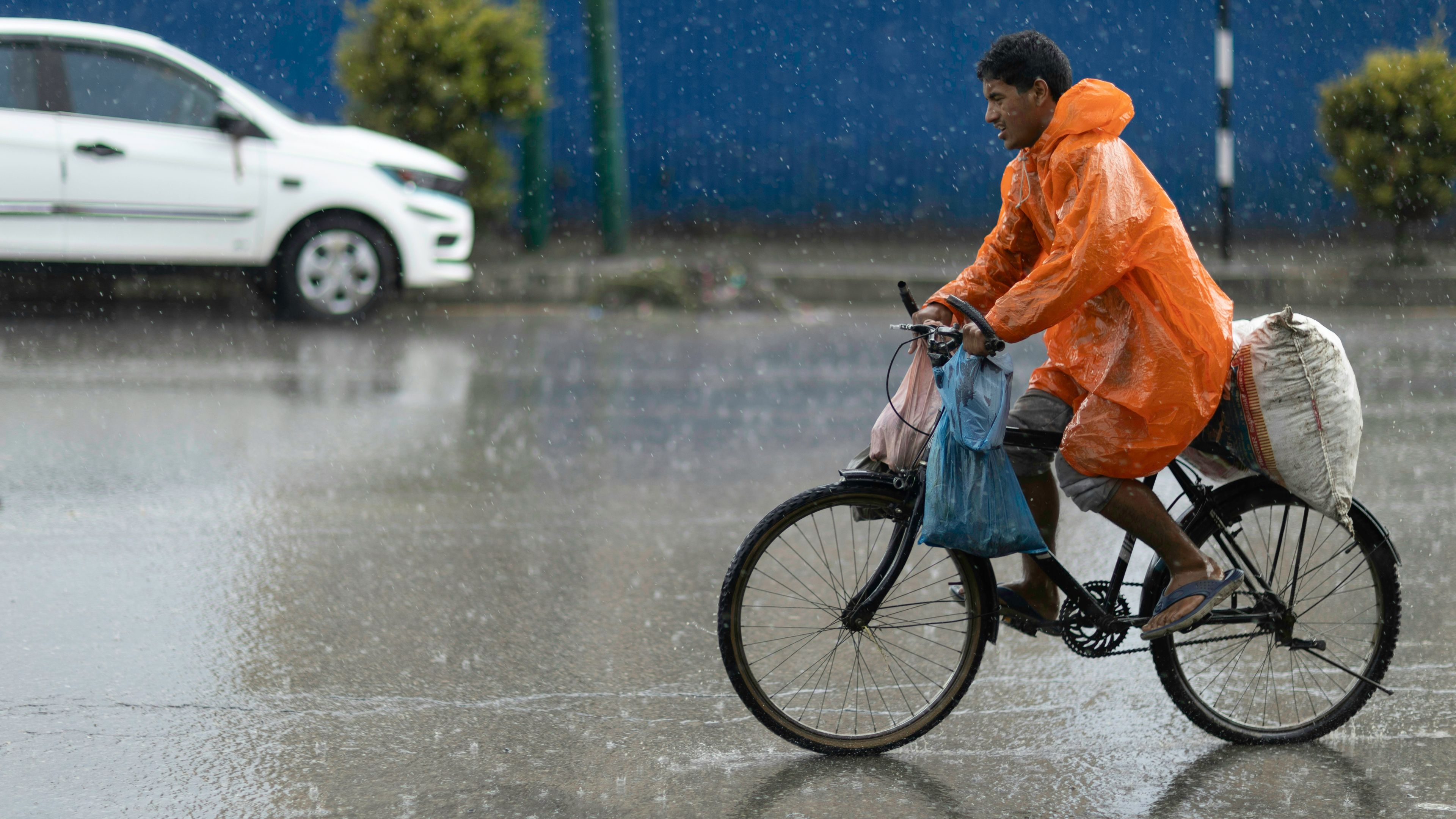 Man in orange raincoat rides bicycle through heavy rain.