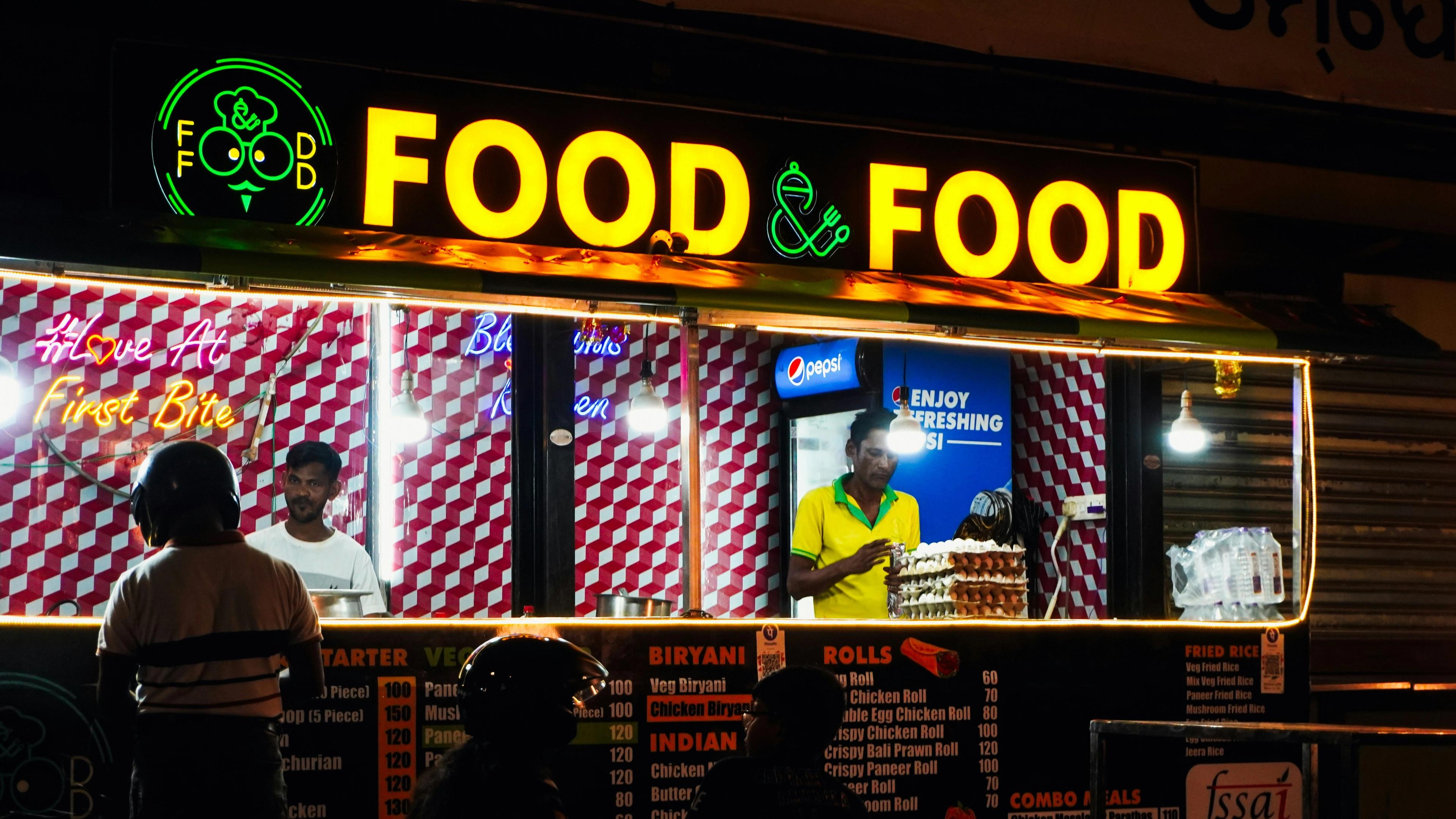 Food stall with bright "food & food" sign at night