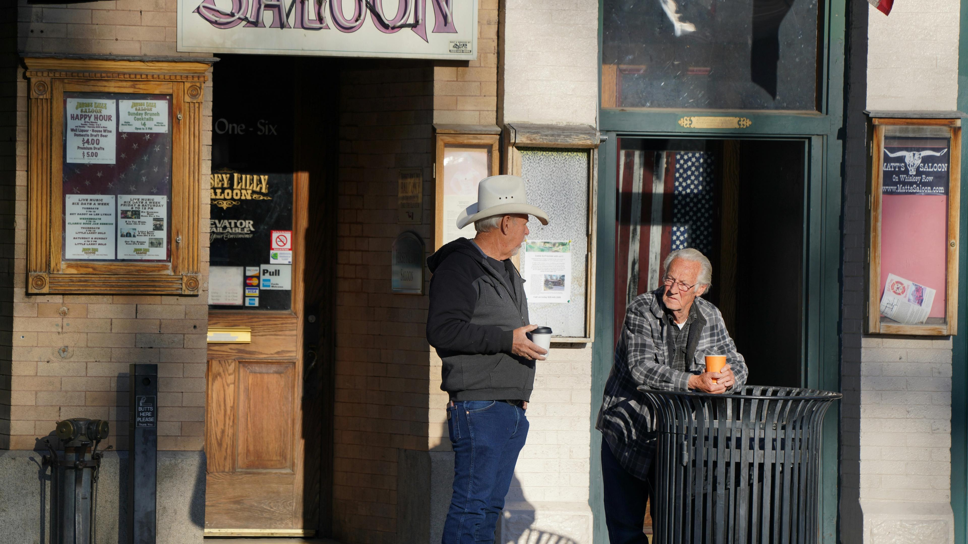 Two men stand outside a saloon chatting