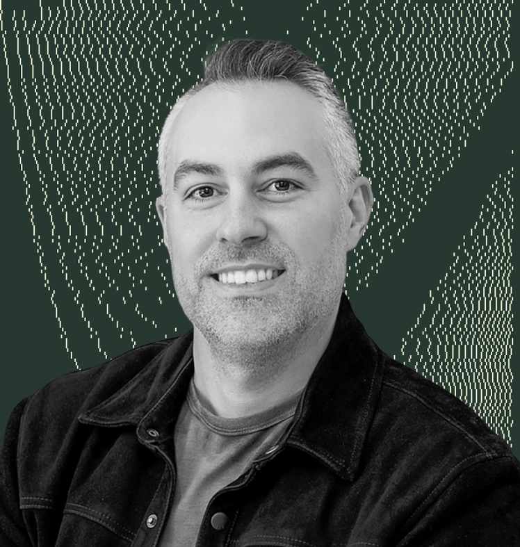 Marcel Santilli in a black jacket is smiling in front of a green background