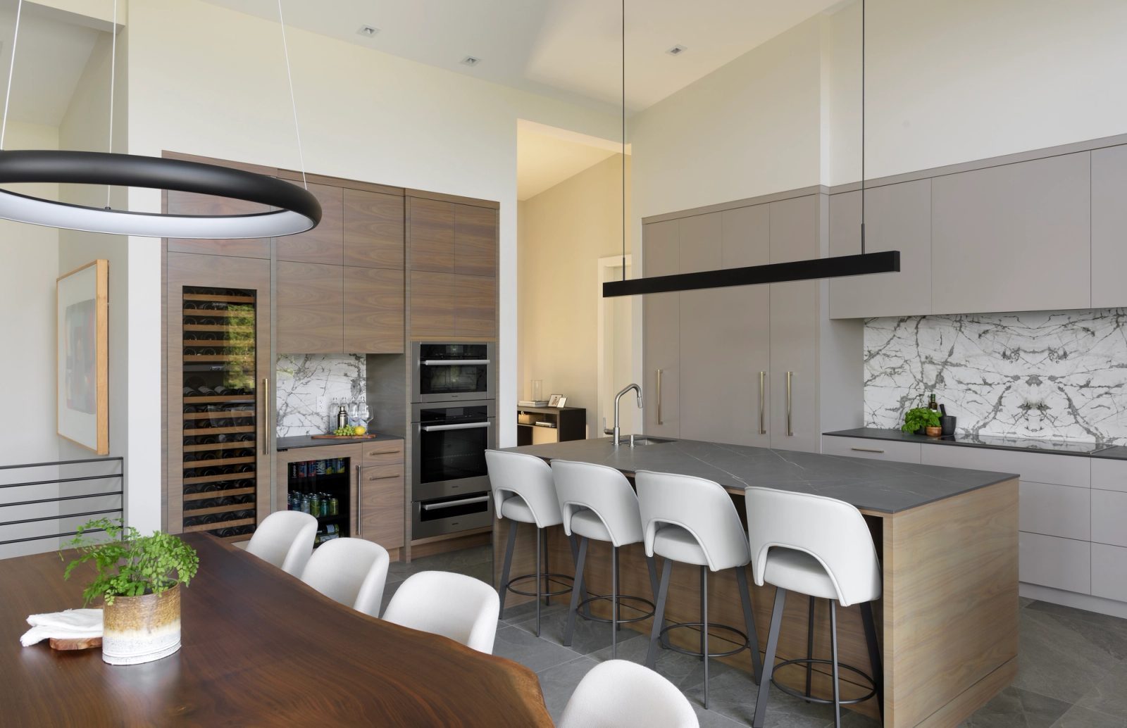 Kitchen with walnut cabinetry, a tall wine cabinet, double ovens and a dark stone island seating four