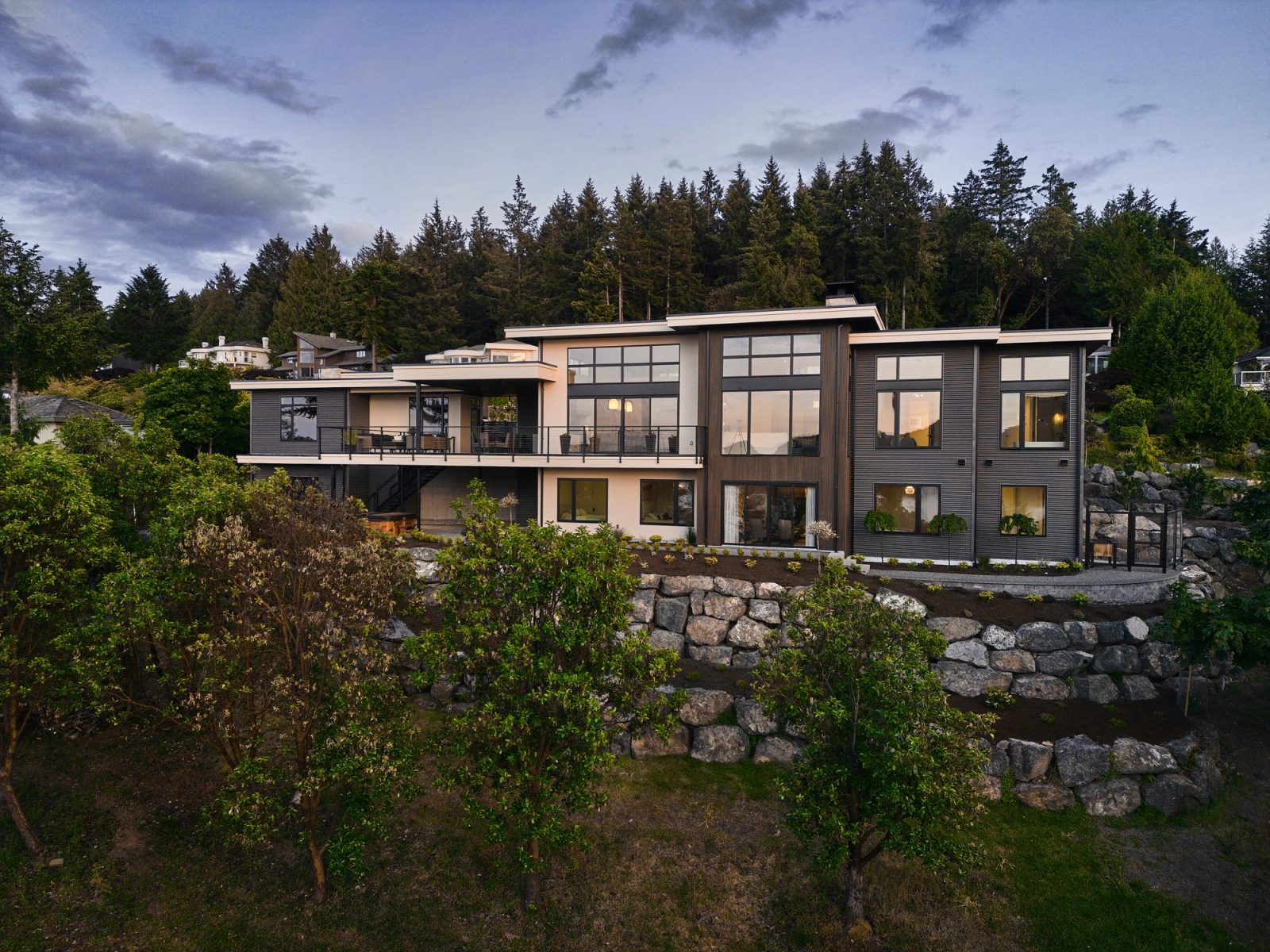 Rear elevation at dusk showing two full storeys, windows lit above the rock retaining walls