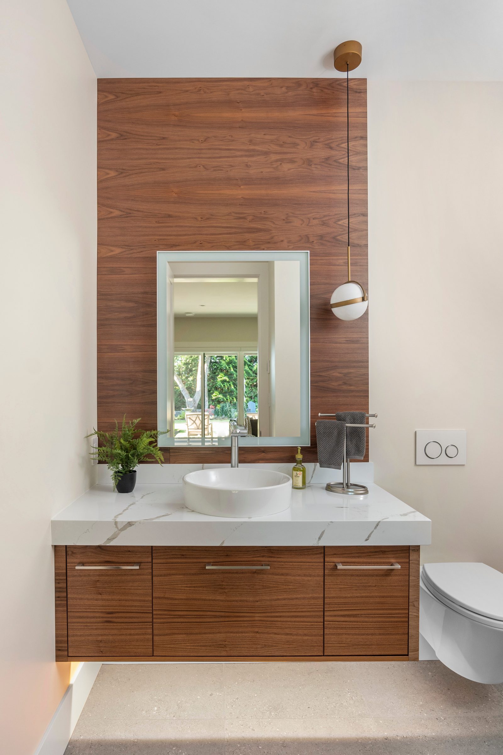 Powder room with a walnut feature wall, a vessel basin on quartz and a brass pendant