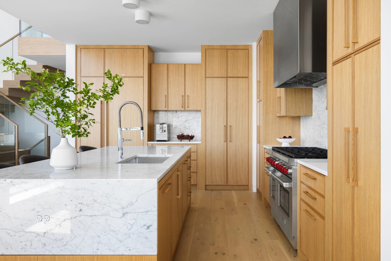 Kitchen looking down the length of the island to a range under a stainless hood, with oak cabinetry on both sides.