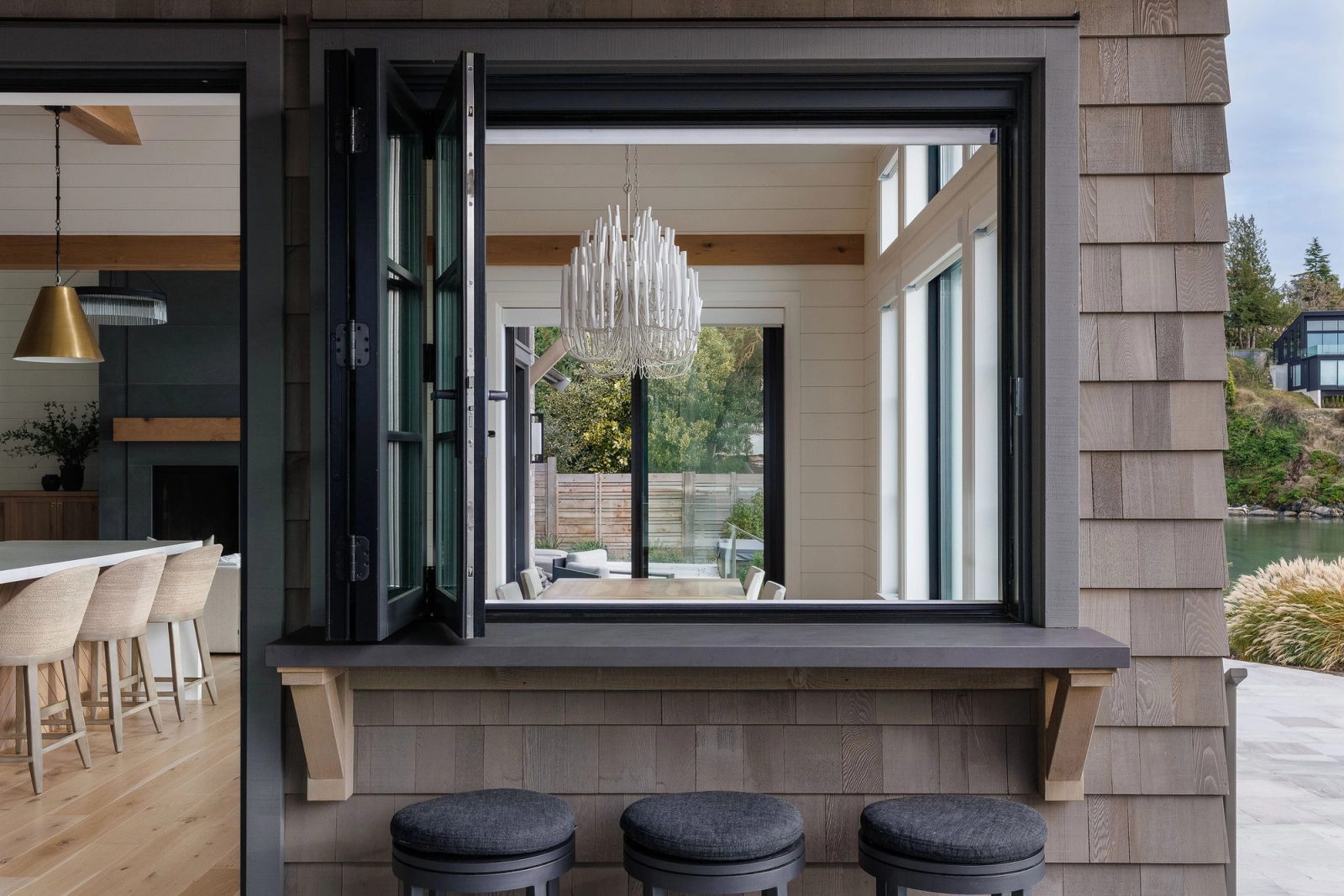 A folding window opens the kitchen onto a terrace counter with stools, the bay visible beyond