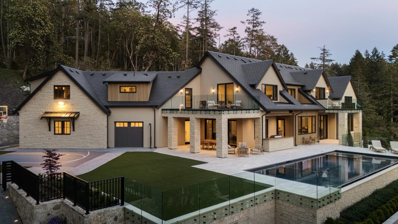 The house at dusk from across the pool, terraces and stone retaining walls stepping down to the water, forest closing behind.