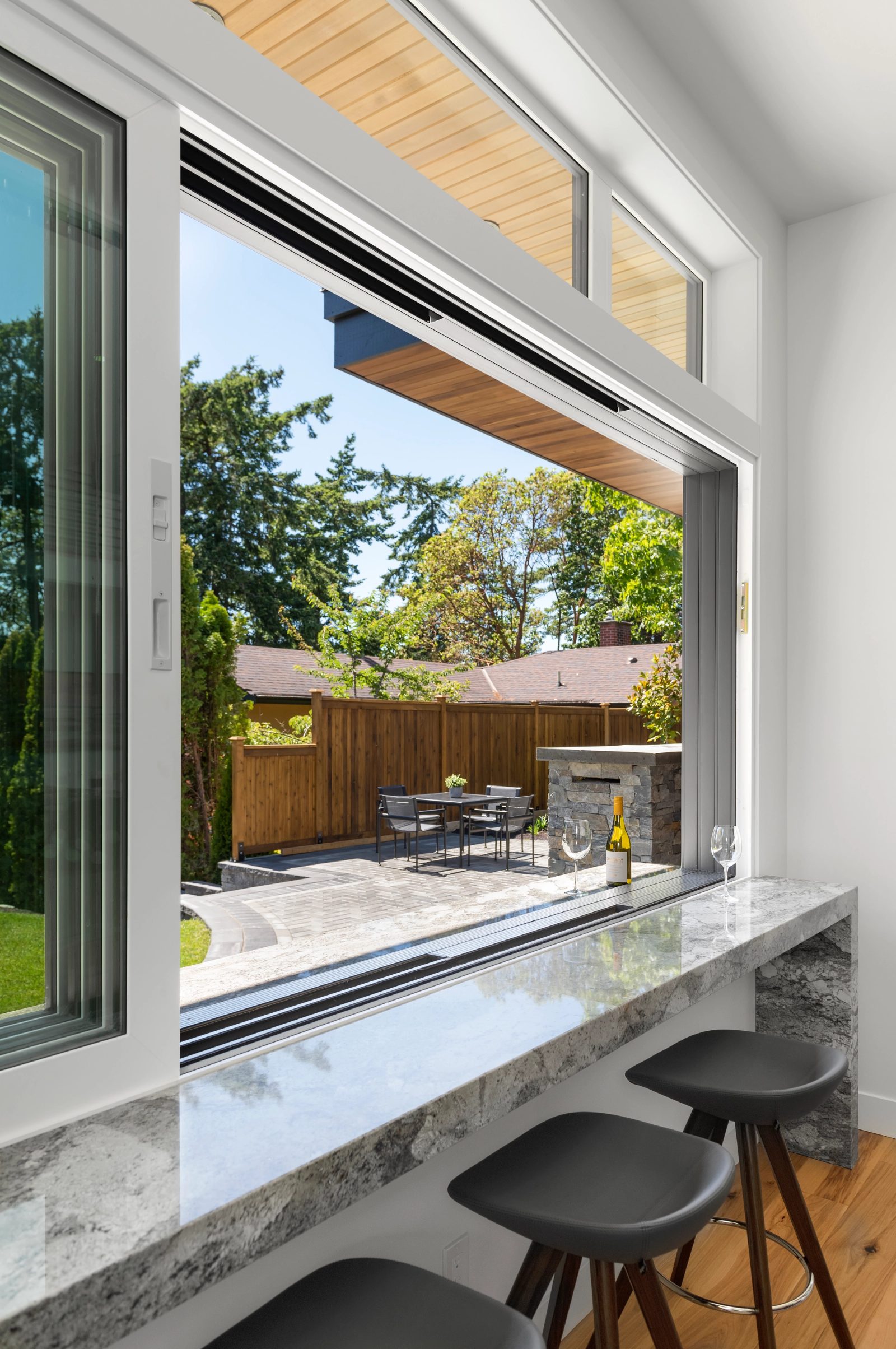 Quartzite counter passing through an open window to a covered patio with a dining table and outdoor kitchen