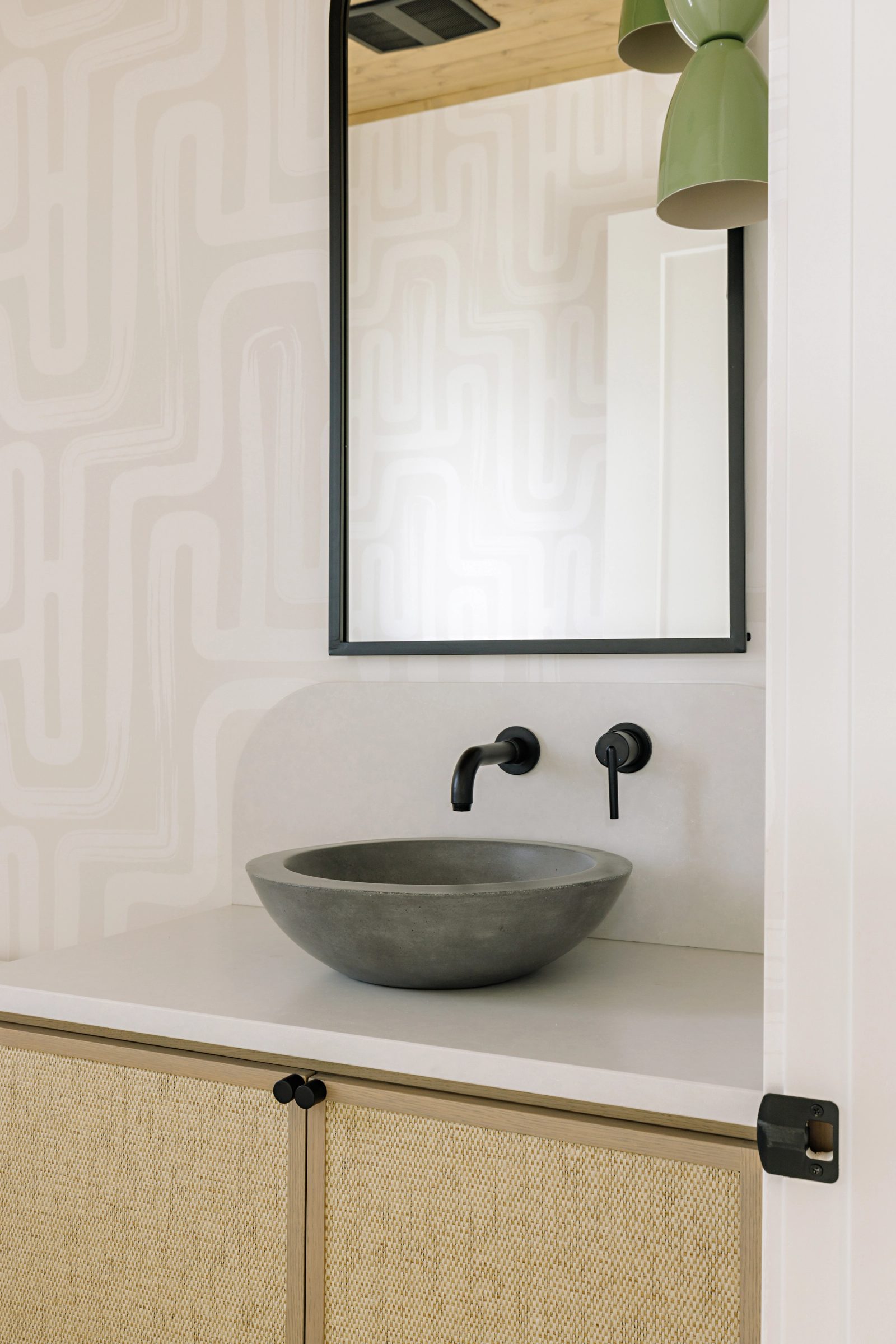 a round concrete basin on a pale counter below a black-framed mirror, against wallpaper printed with soft looping lines.