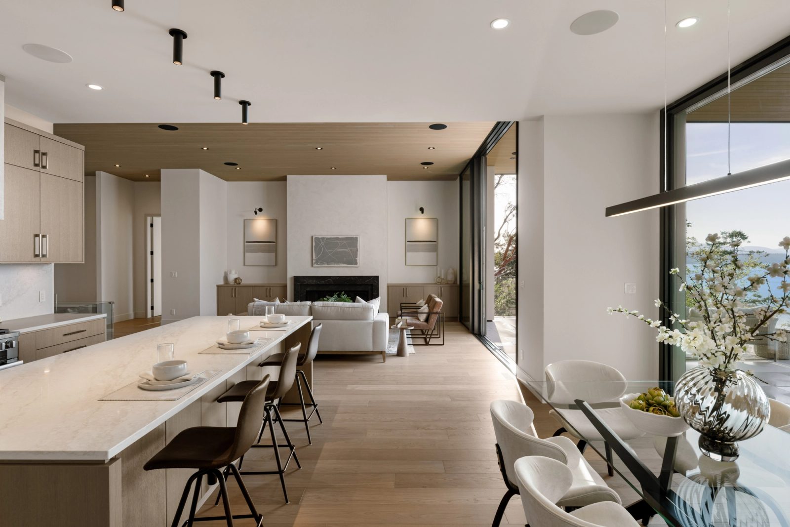 The length of the kitchen island toward a seating group and fireplace, a glass dining table and the open terrace wall on the right.