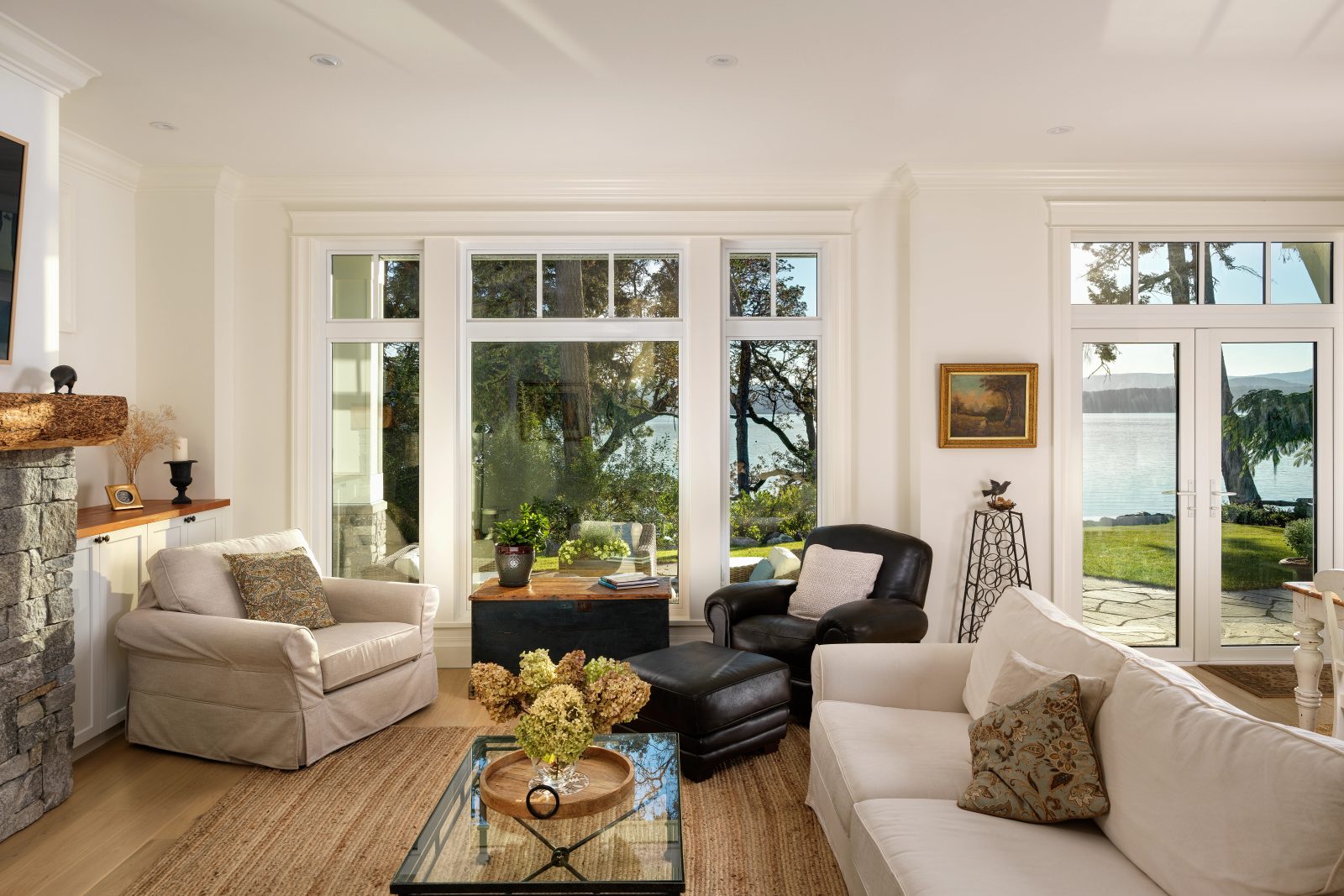 Living room looking out through paired doors and transom windows to a stone patio, lawn and water beyond.