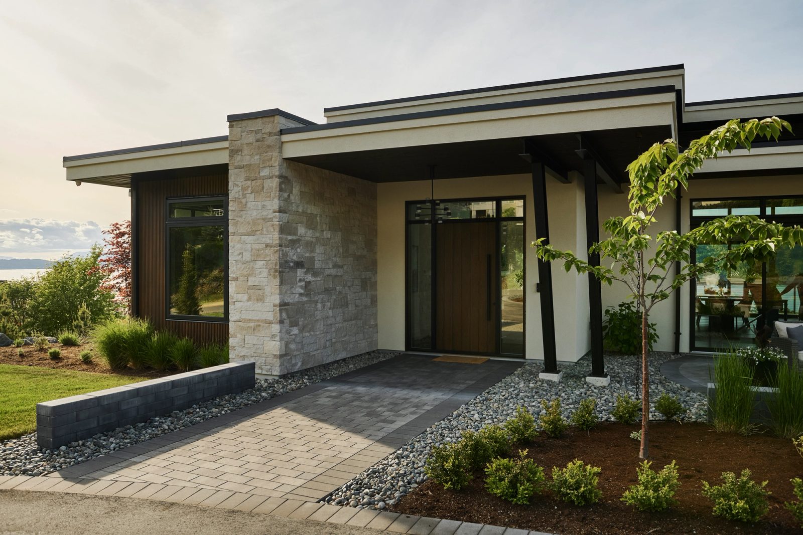 Covered entry with stacked stone pier, timber door and black steel posts over paver walk