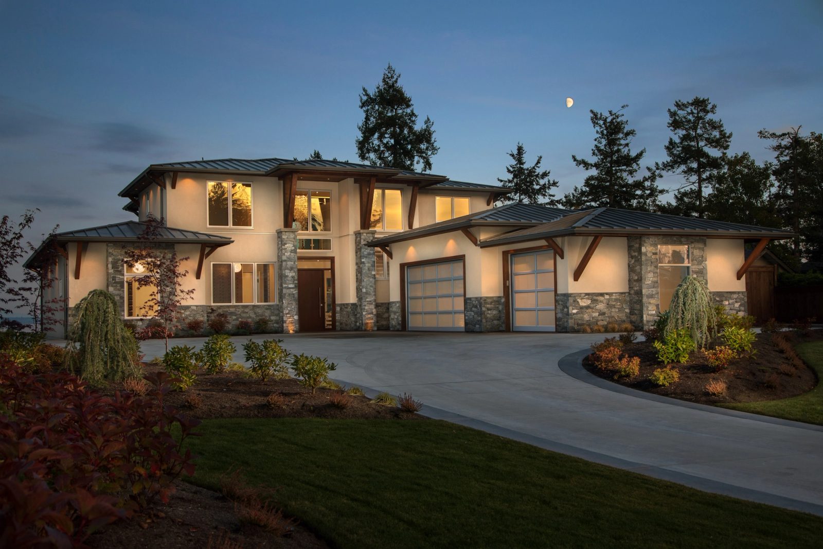 Contemporary house at dusk with lit windows, timber brackets and a stone base under a rising moon