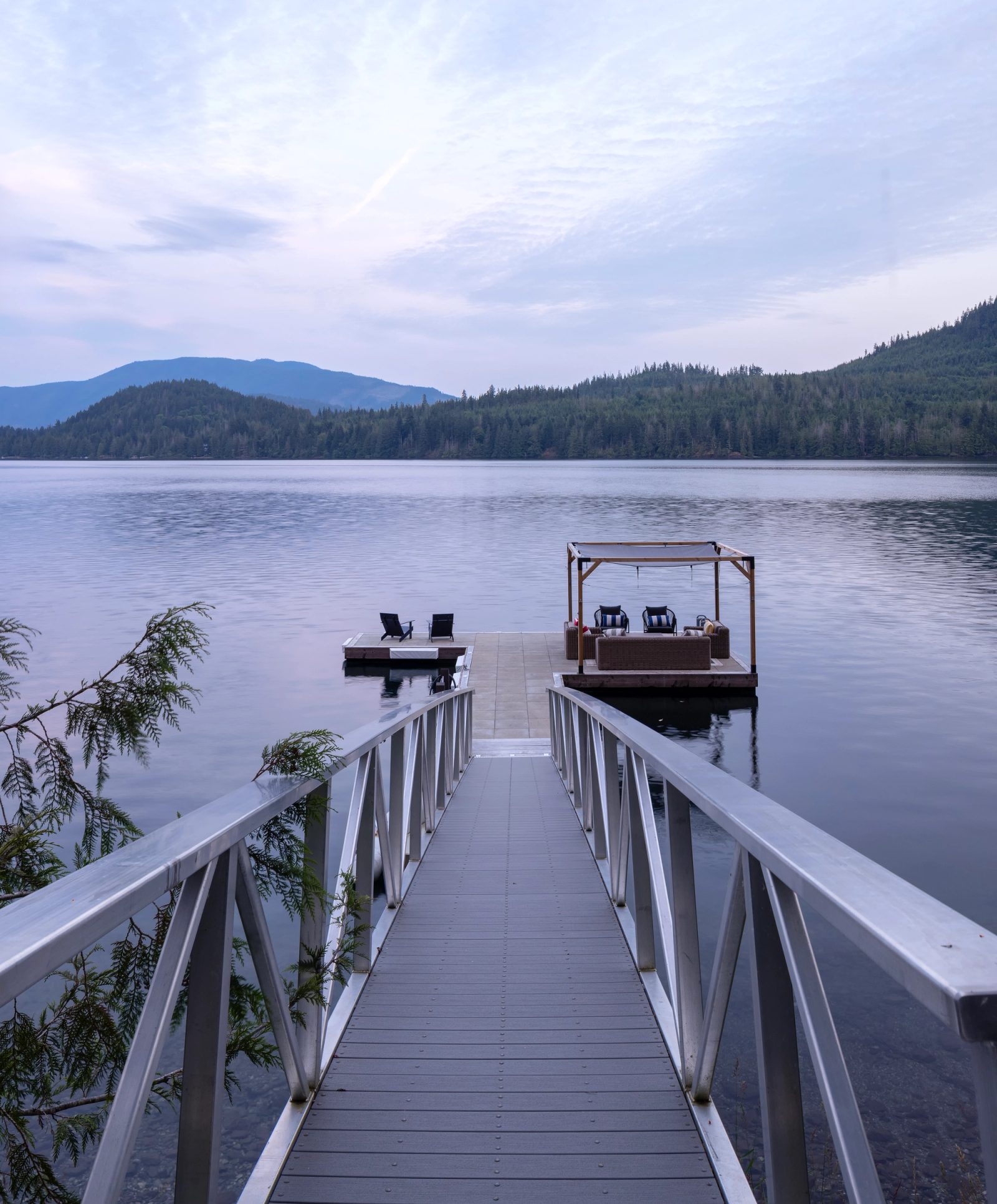 Aluminium ramp running out to a floating dock on still water at dusk, forested ridges beyond