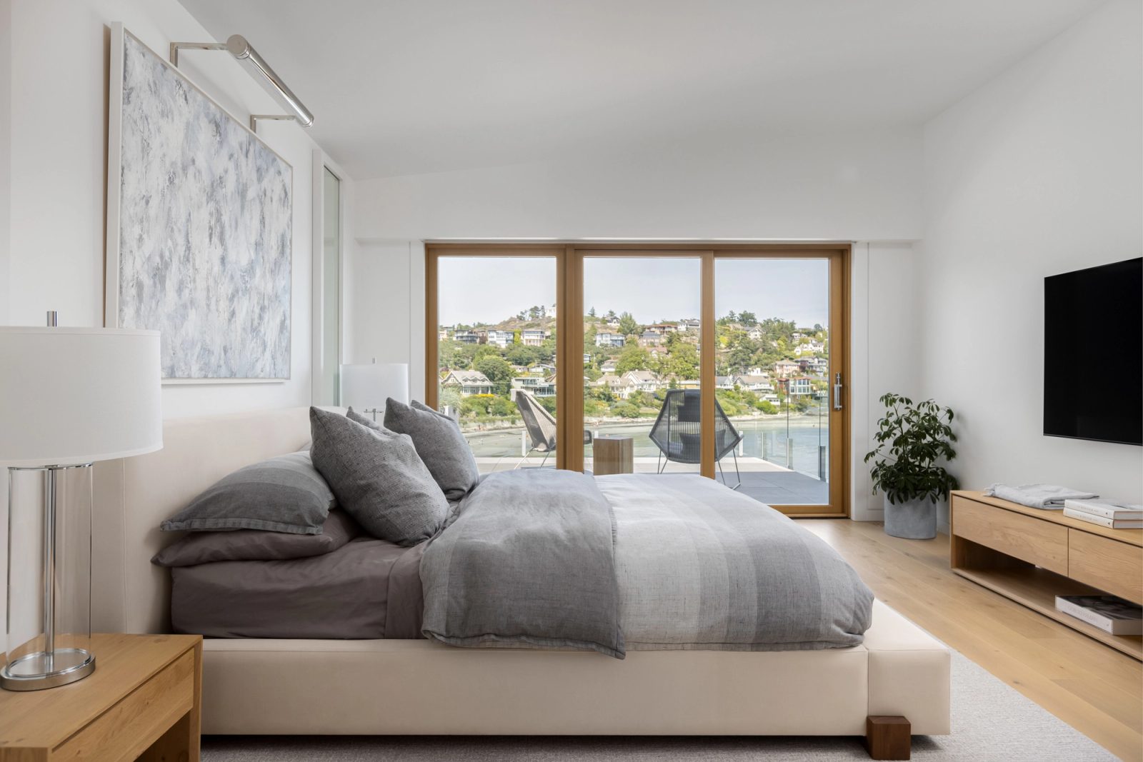 Bedroom with a low upholstered bed, grey linen, and sliding doors to a balcony above the beach.