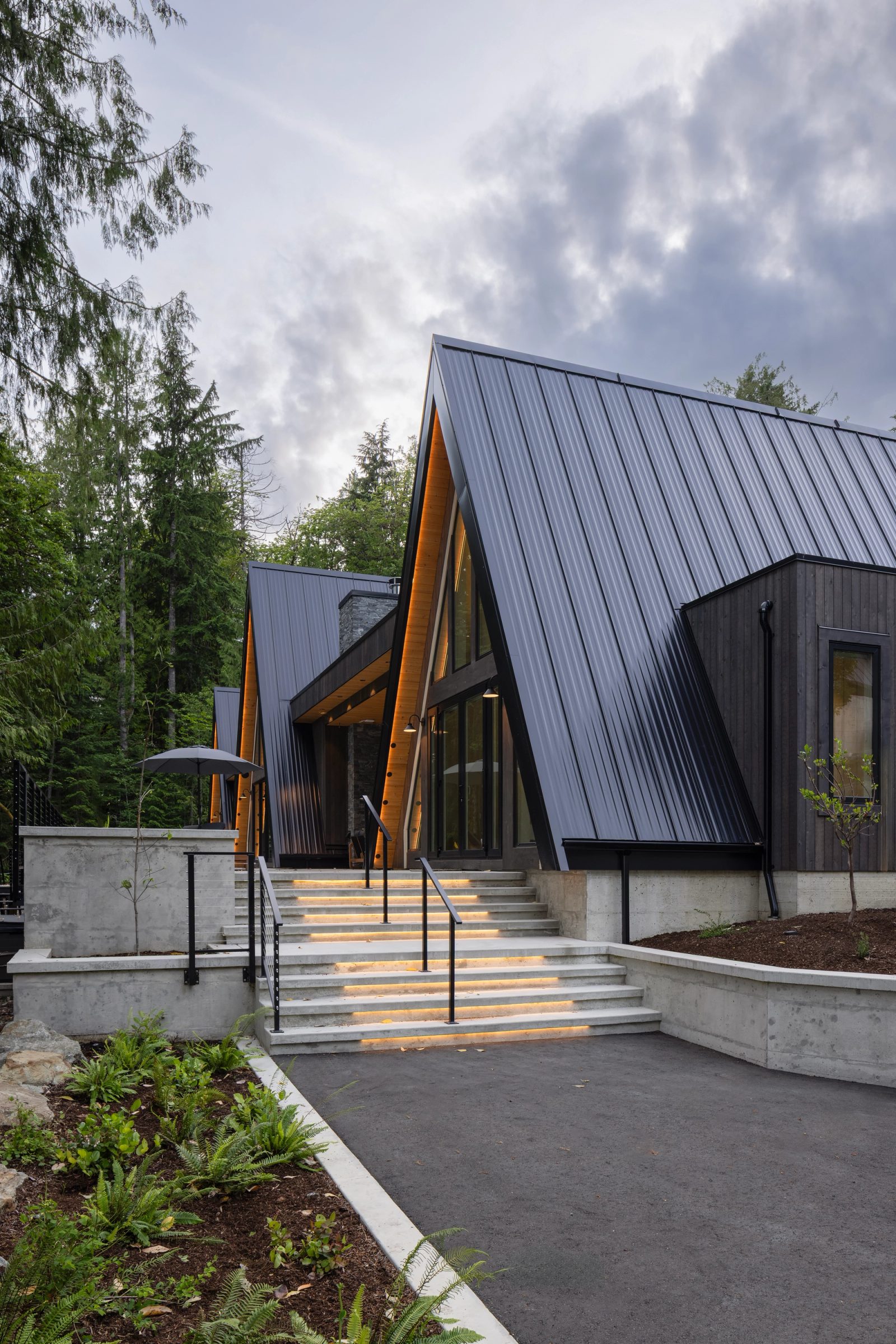 Lit concrete steps rising to a black A-frame entry under an overcast sky