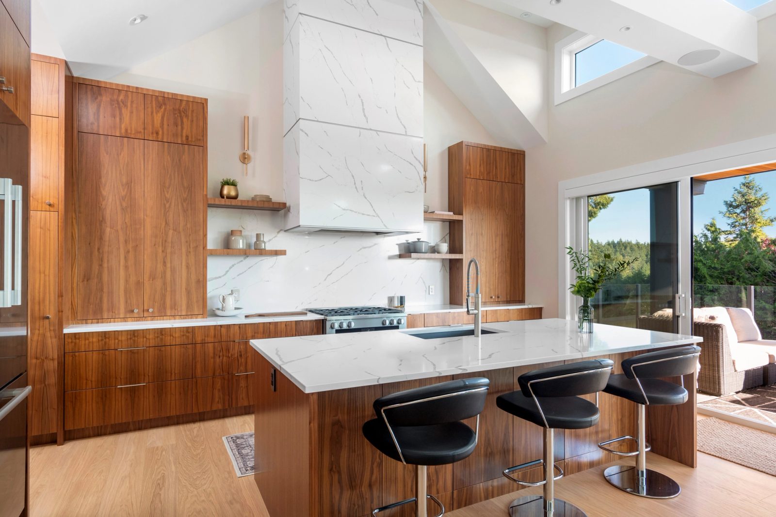 Kitchen under a vaulted ceiling with walnut cabinetry, a quartz hood and sliding doors to the deck