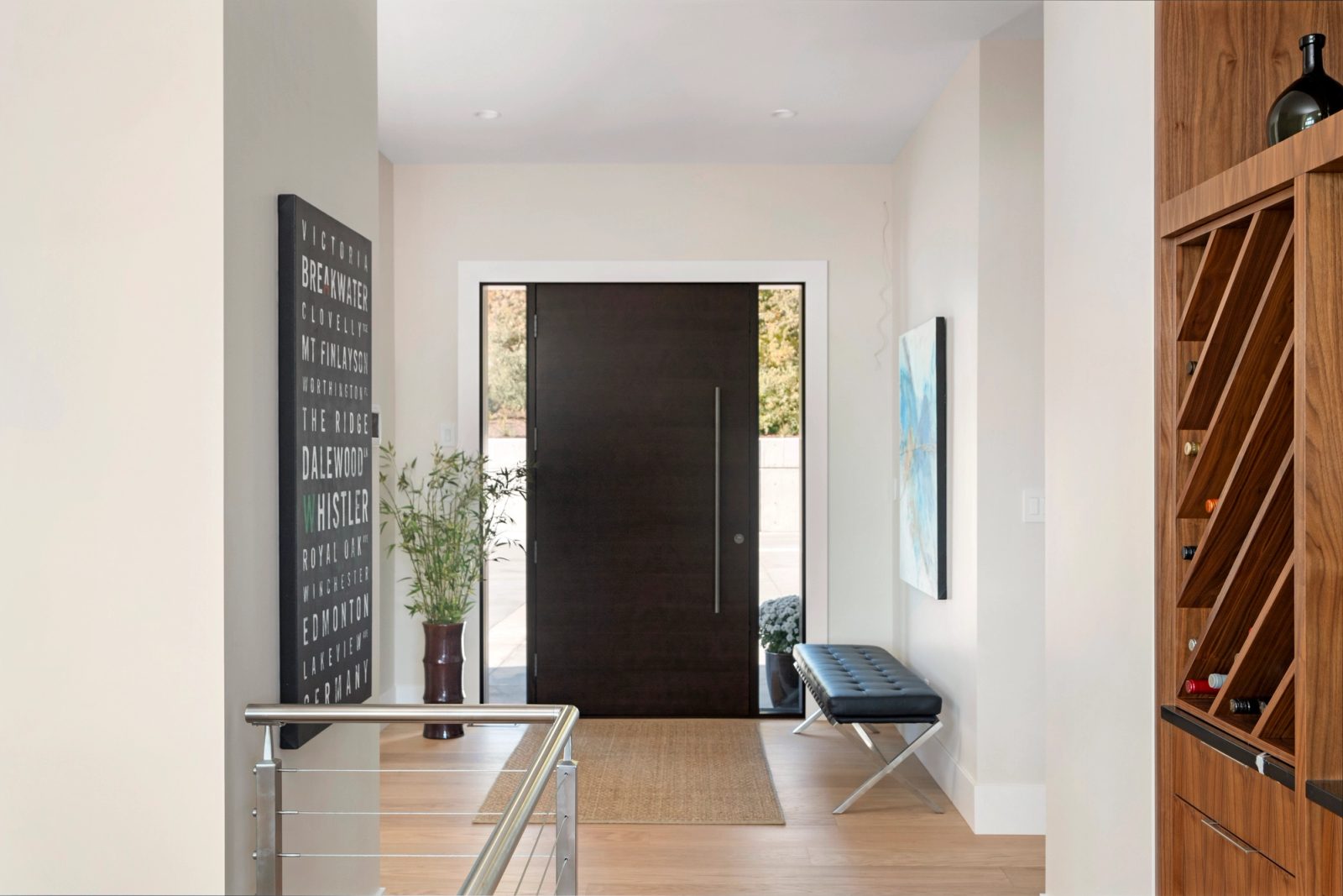 Entry hall with a dark flush front door, a walnut wine wall and a cable-railed stair descending