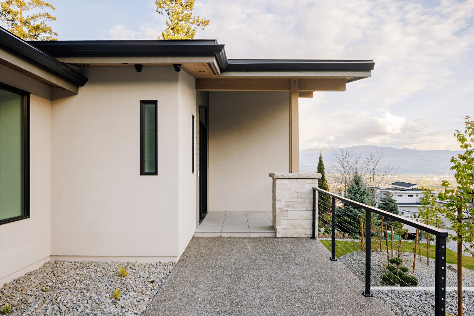 A covered entry at the corner of the house opening onto the valley, the city and the far mountains laid out beyond a cable rail.