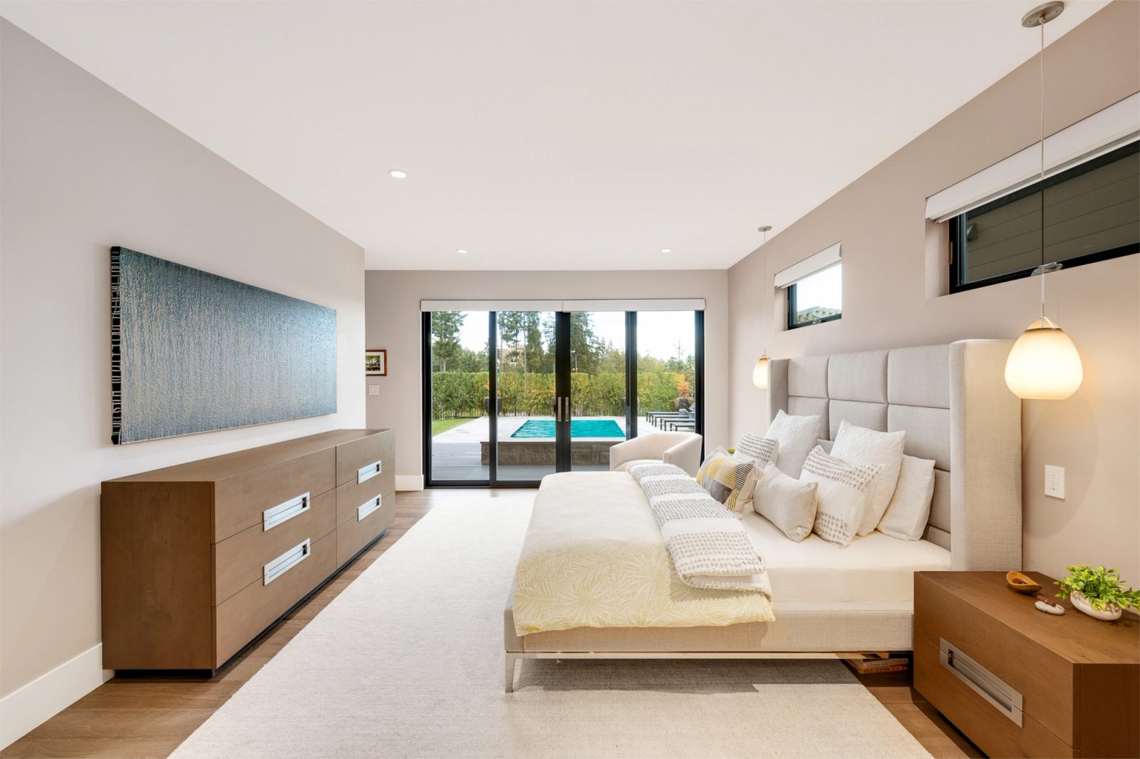 Primary bedroom on the lower floor with sliding doors opening at grade to a pool deck and clipped hedge