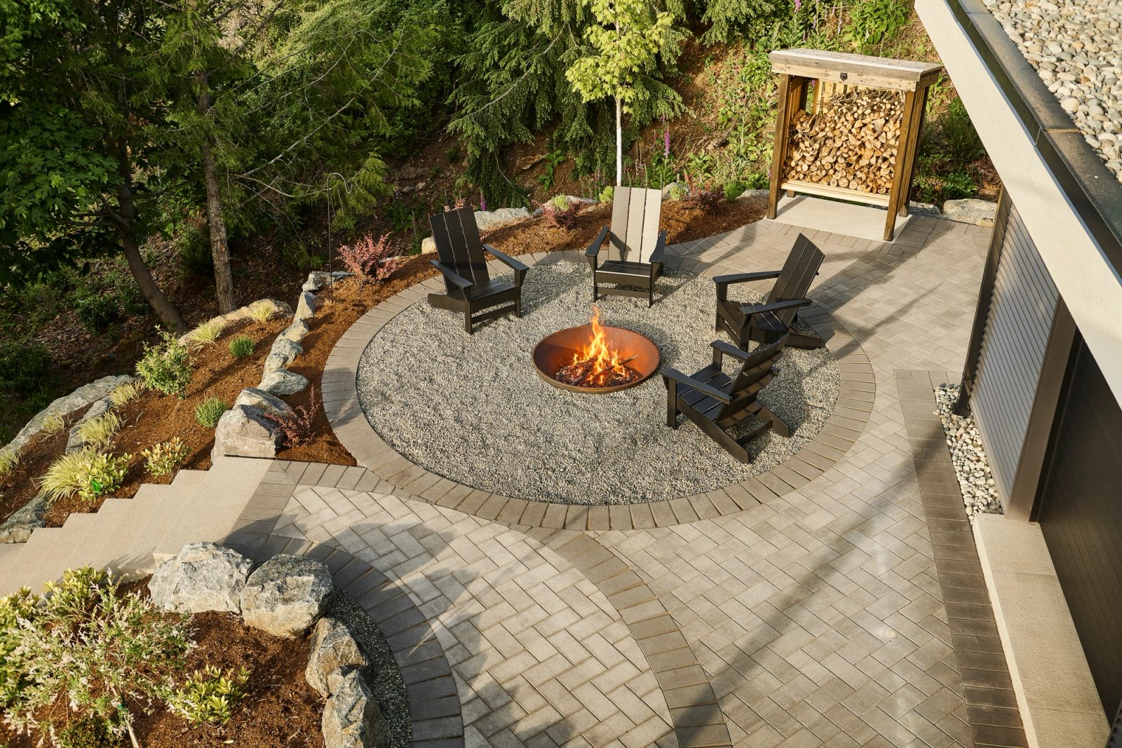 Fire pit terrace in herringbone paver and gravel, cut into the slope above the trees