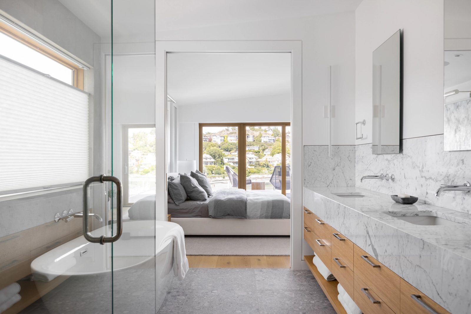Ensuite with a marble vanity on oak drawers and a glass shower, looking through a wide opening to the bedroom beyond.