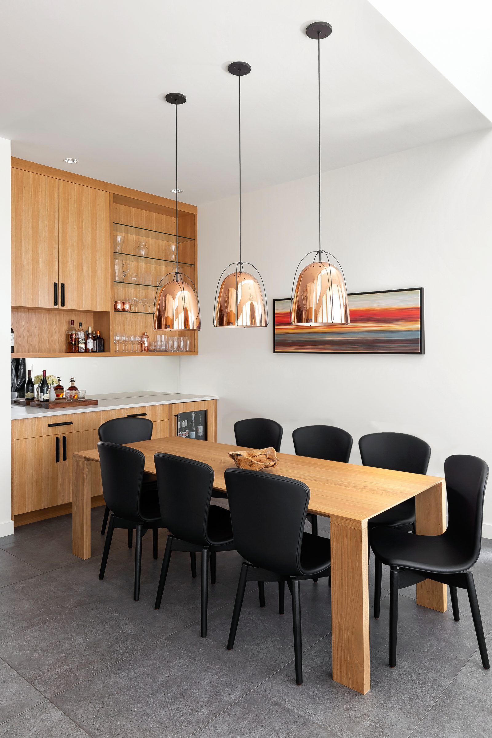 Dining table under three copper pendants beside an oak bar cabinet