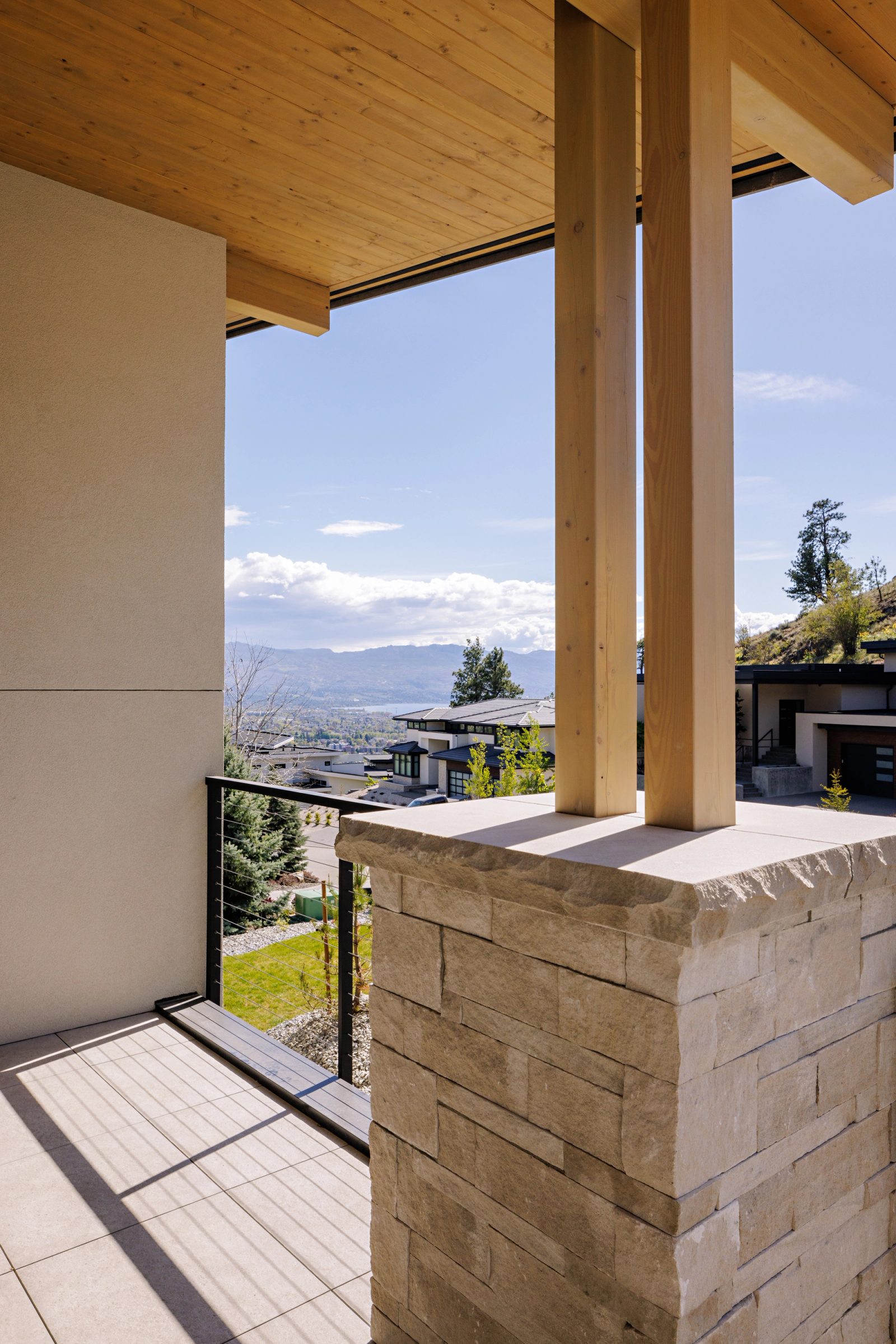 a covered terrace looking out between timber posts and a stone parapet to the valley and distant water.