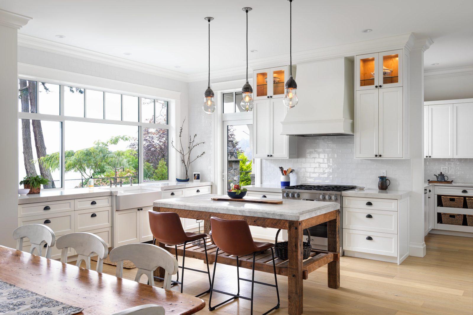 Kitchen with white shaker cabinets, a marble-topped reclaimed wood island, three glass pendants and a long window above the sink.