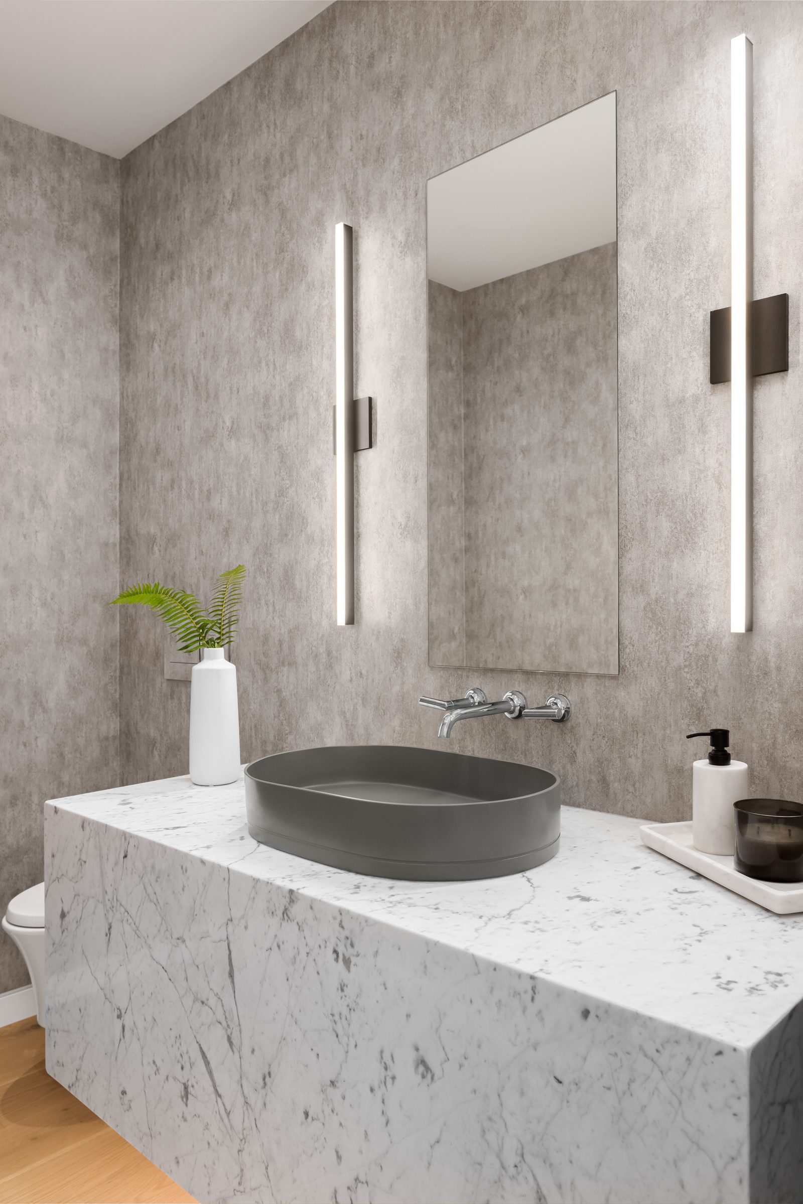Powder room with a grey basin set on a marble block, a slim mirror and two vertical light bars.