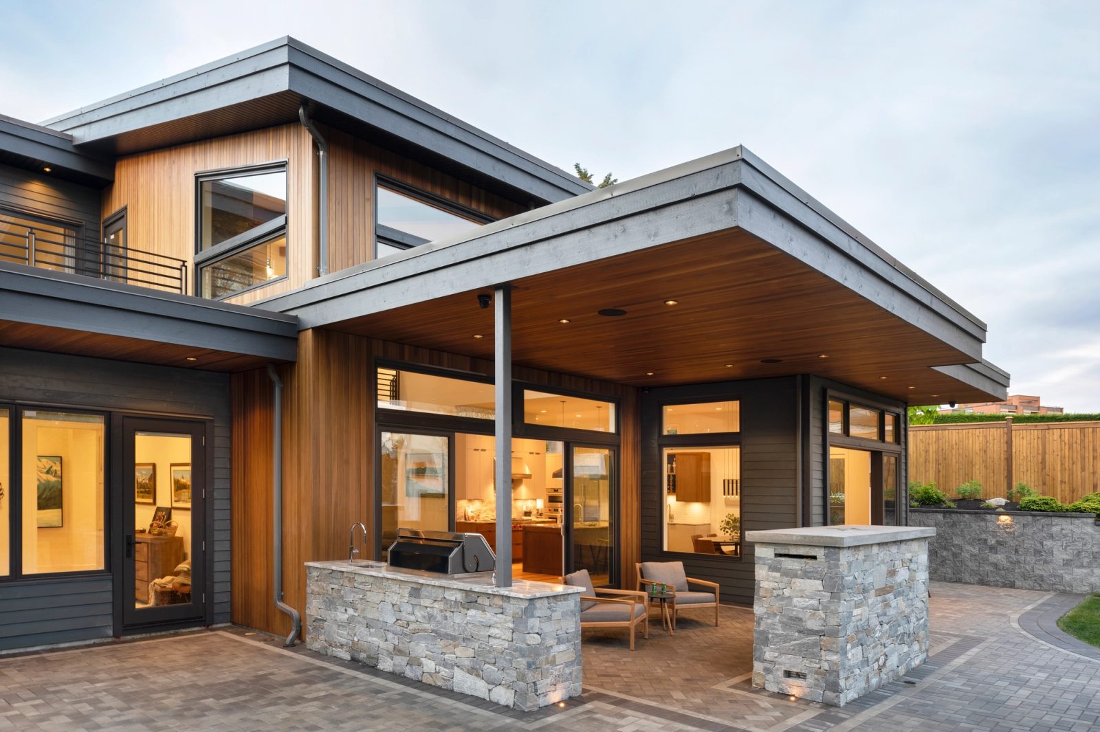 Covered patio at dusk with a stone outdoor kitchen, seating and sliding doors open to a lit interior