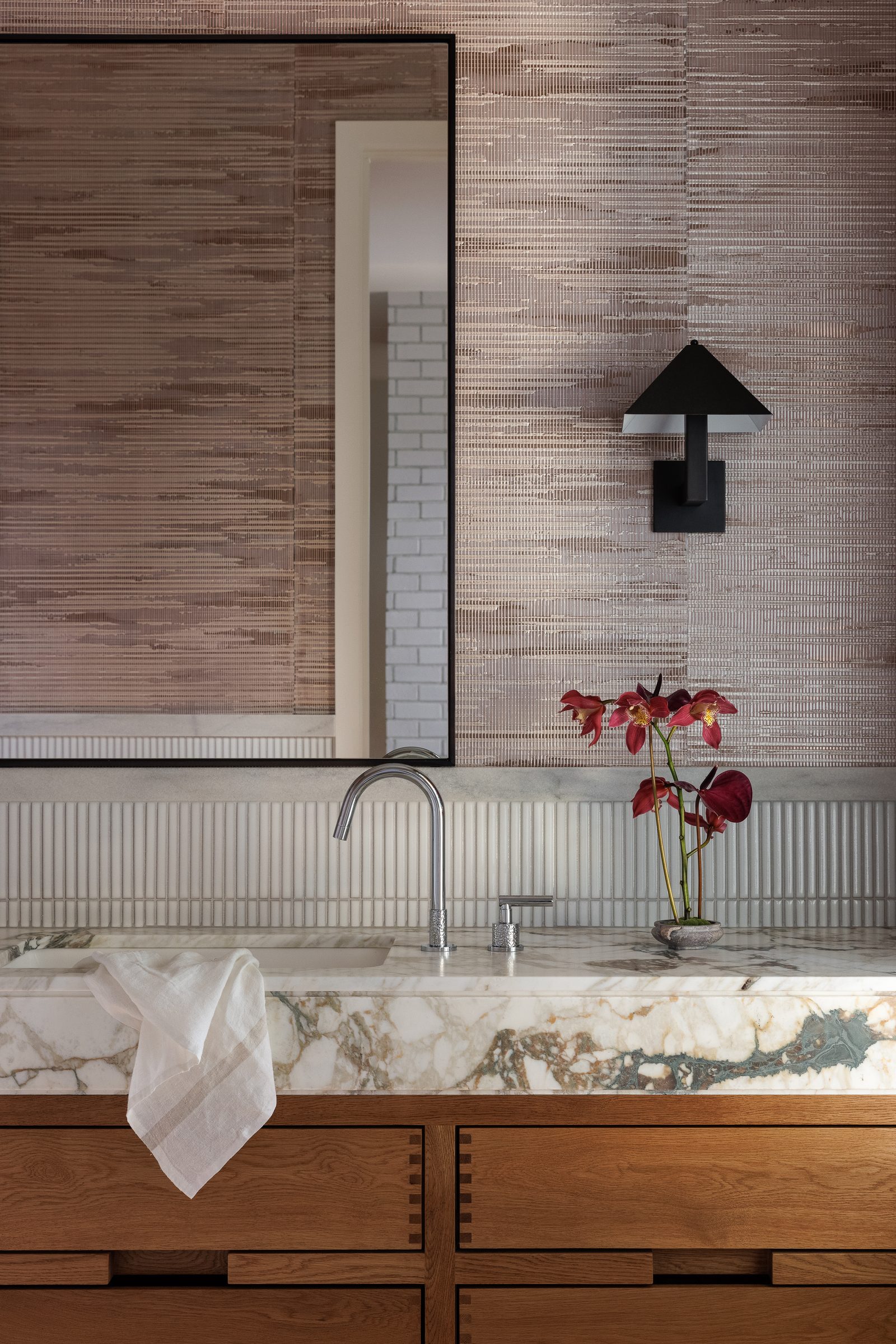 Right: the same vanity closer, a veined marble counter above oak drawers, against grasscloth and a fluted white tile splash.