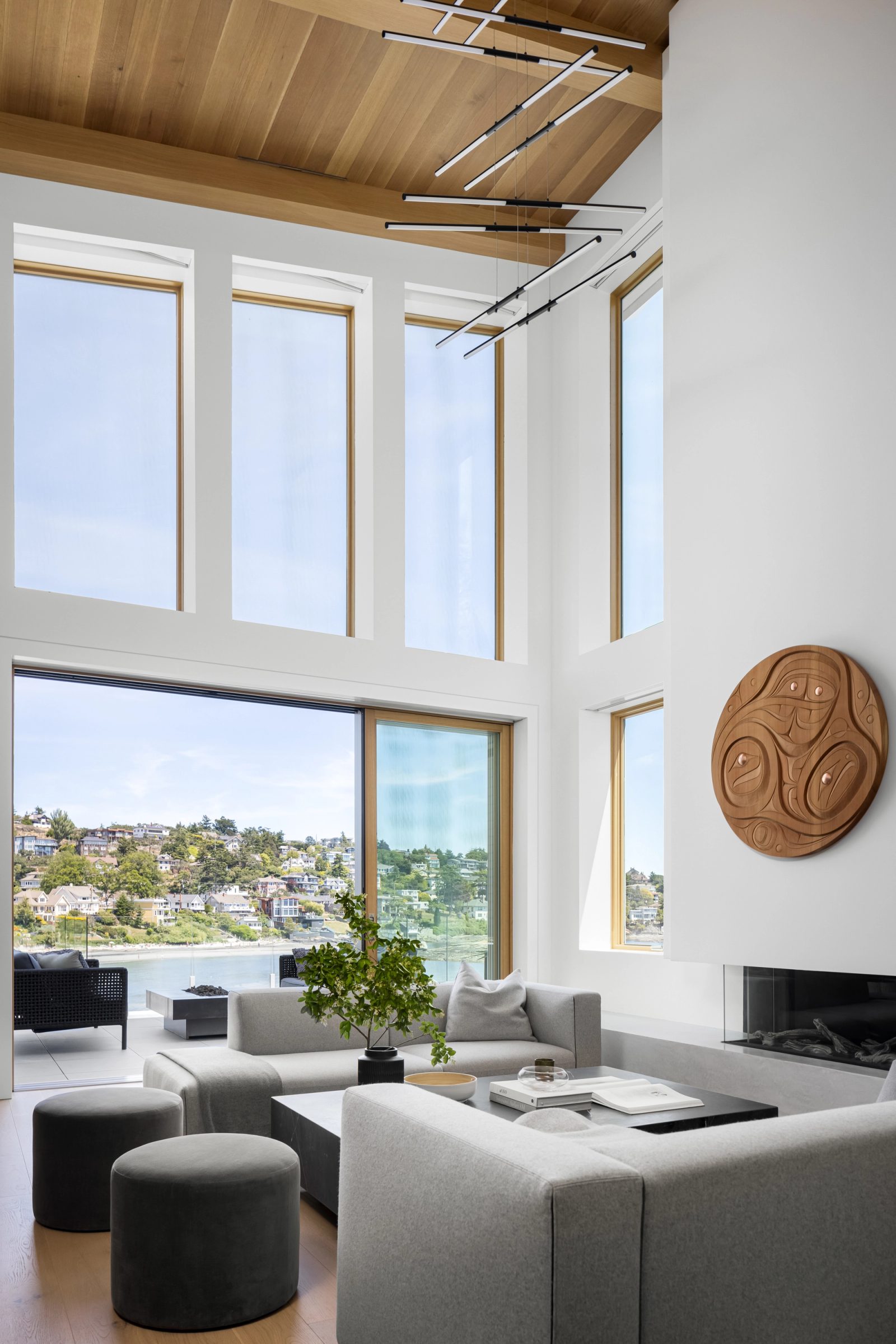 Tall windows and a sliding wall opening from the living room to a terrace, with water and a wooded hillside beyond.