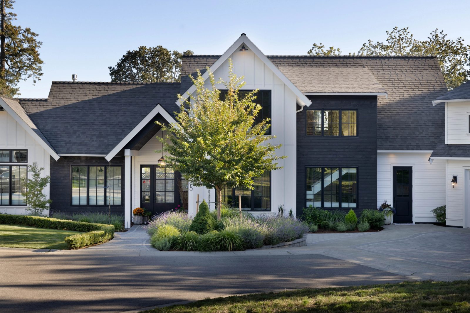 Modern farmhouse with white board-and-batten gables, dark-stained board siding and black-framed windows above a lavender and grass border