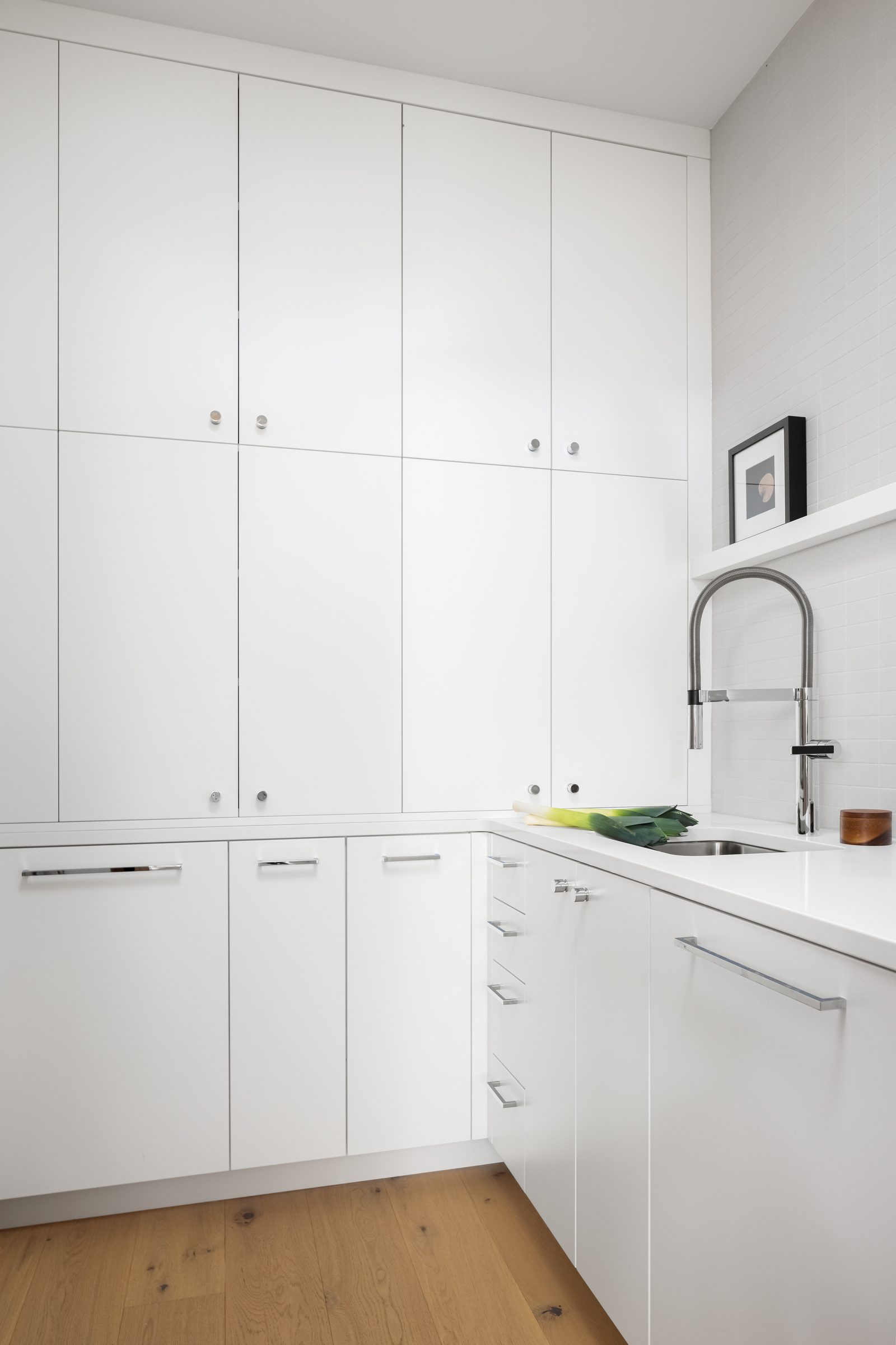 Butler pantry in white cabinetry with a long counter, a tall faucet and a shelf above the sink.