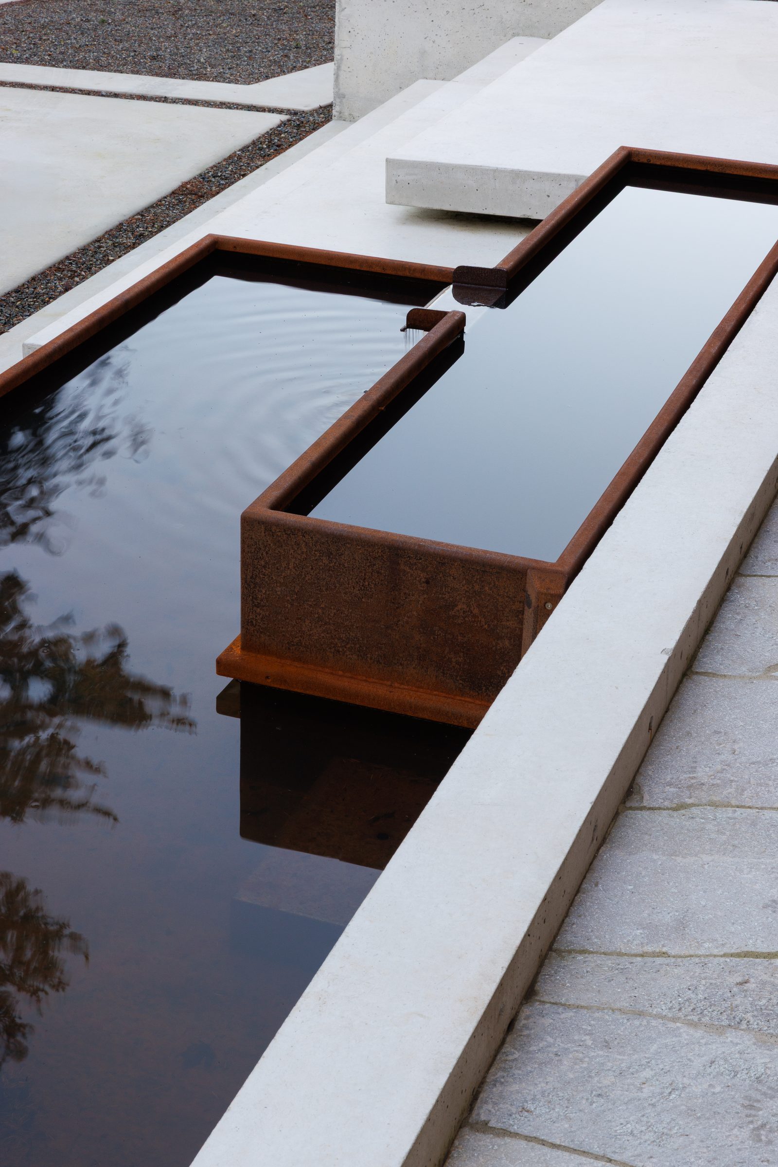 Right: that basin close, two levels of weathering steel spilling into still water against a concrete edge.