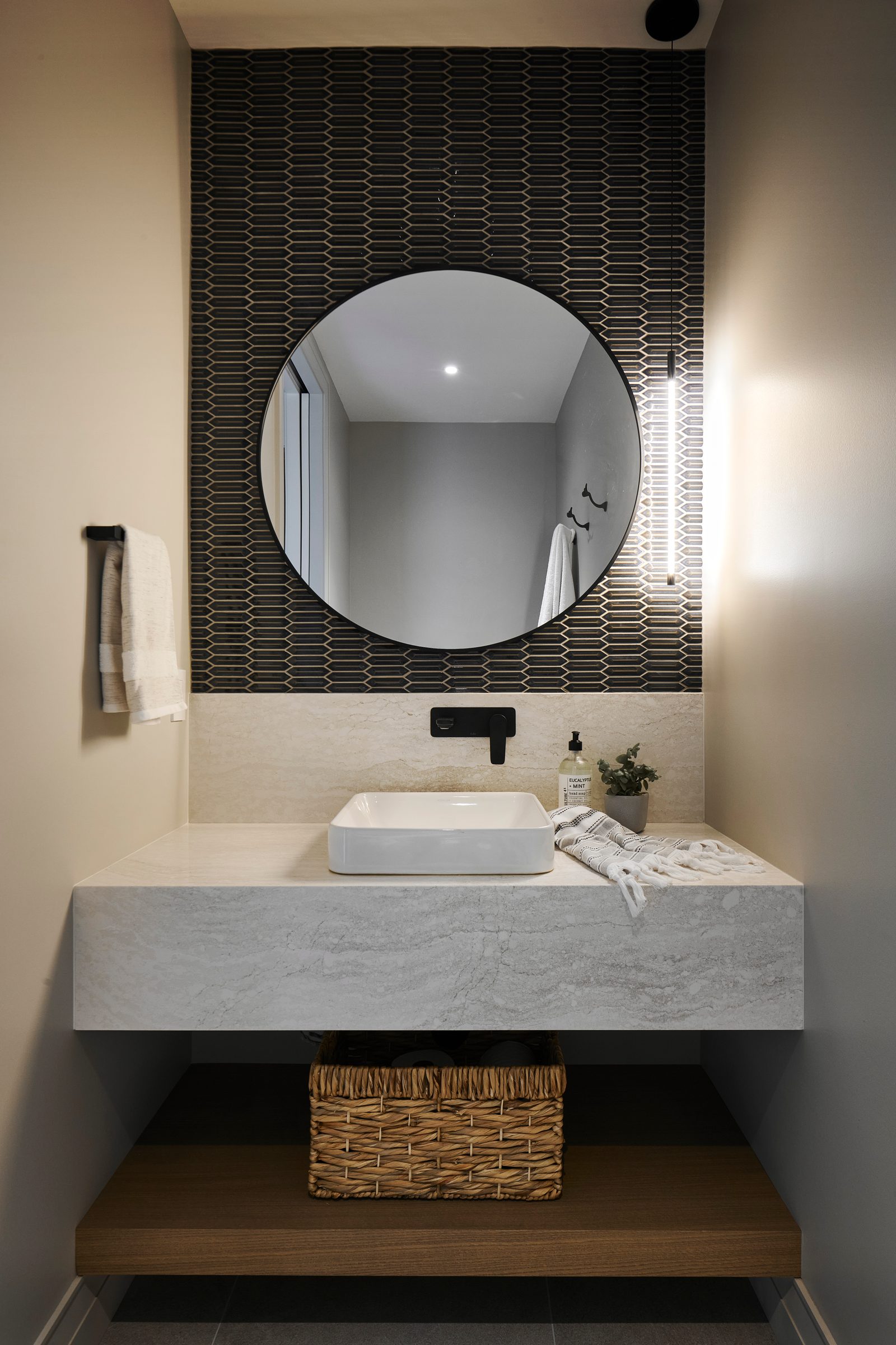 Powder room with black picket tile, round mirror and floating stone vanity