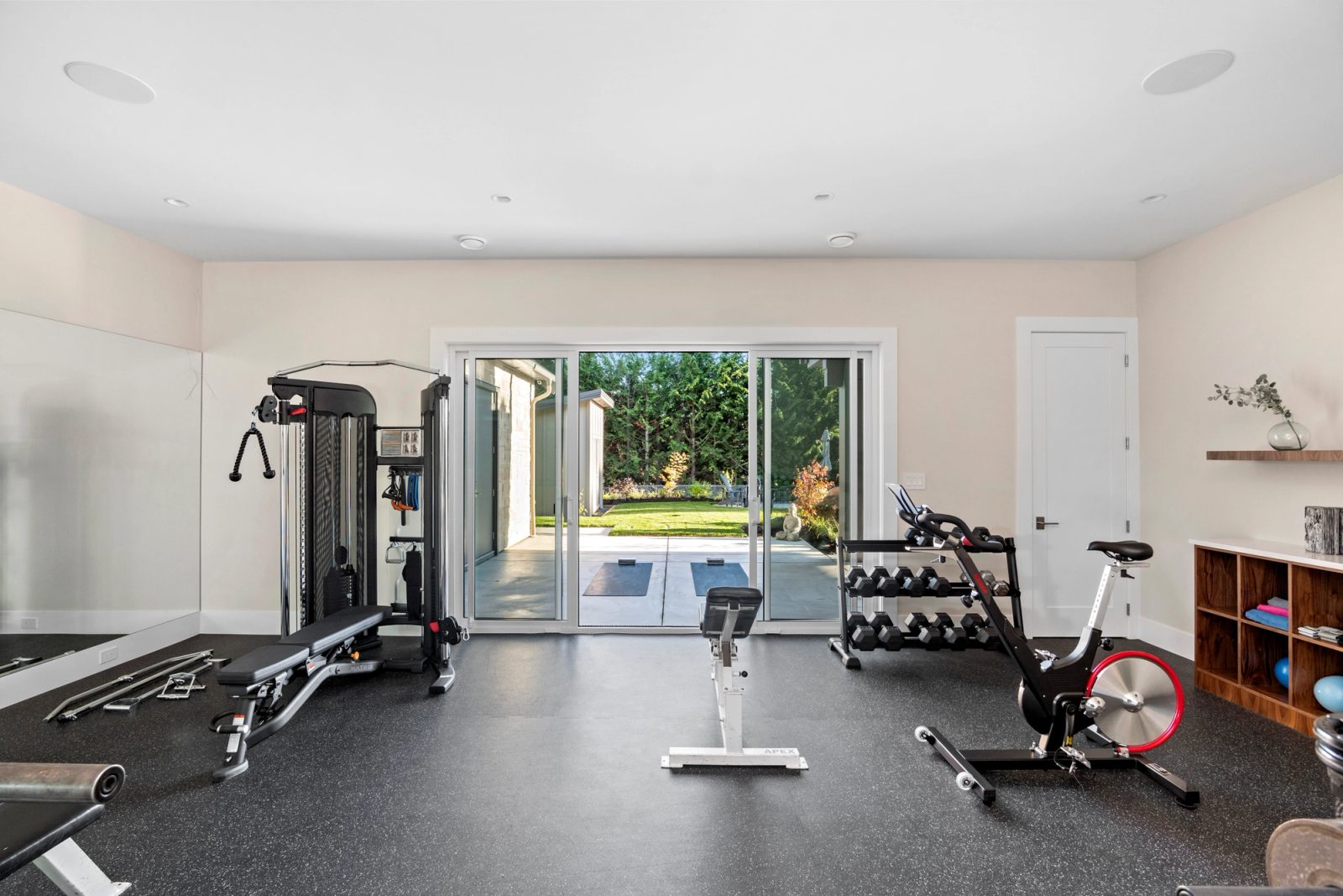 Lower-floor gym with sliding doors open to a concrete terrace and lawn