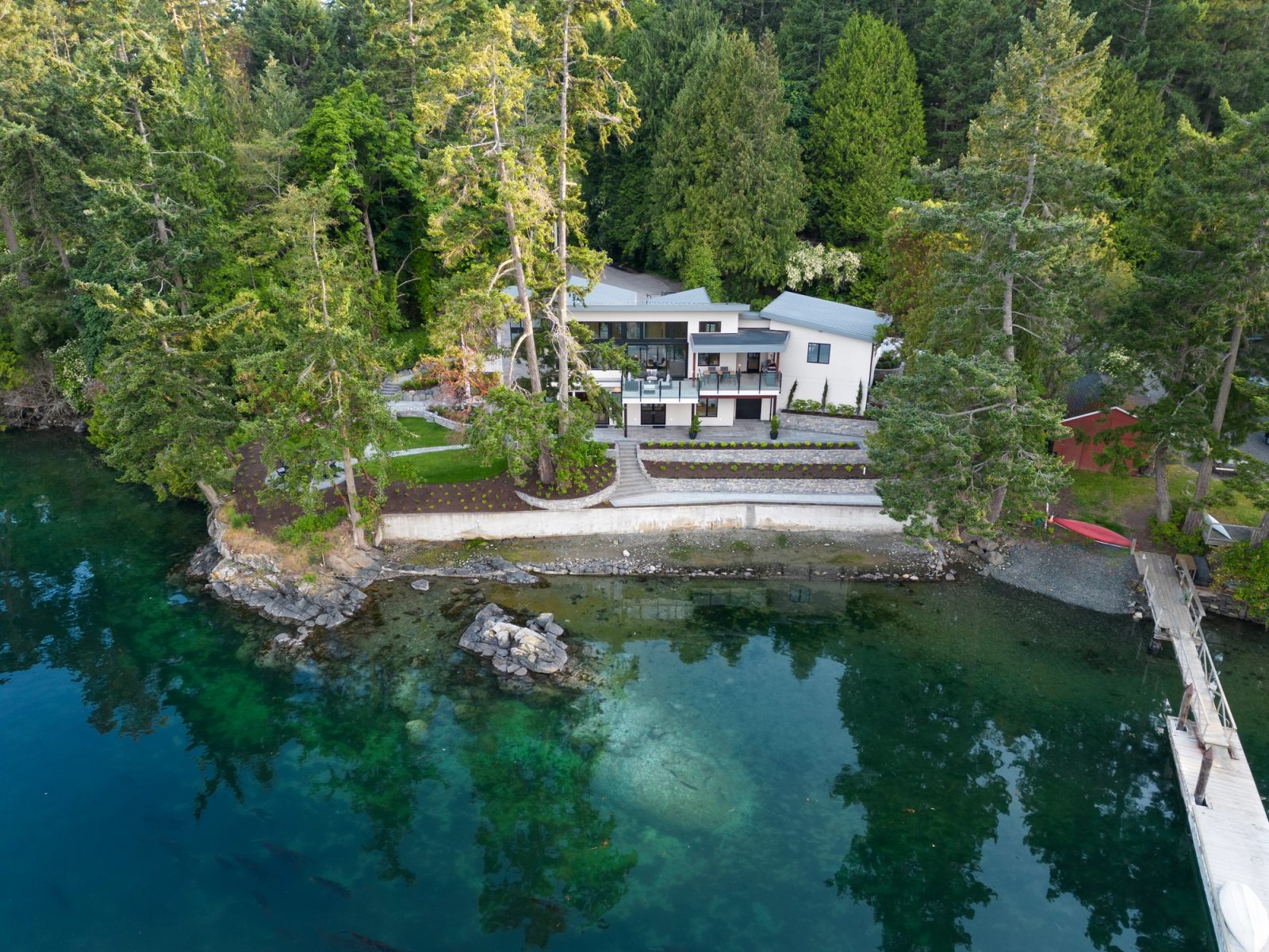 Aerial view from the water of a contemporary waterfront house behind a poured seawall, with a rock shelf exposed at low tide