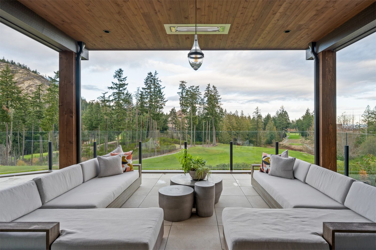 Covered terrace with a cedar soffit and glass rail, looking across the fairway to forest and a rock bluff