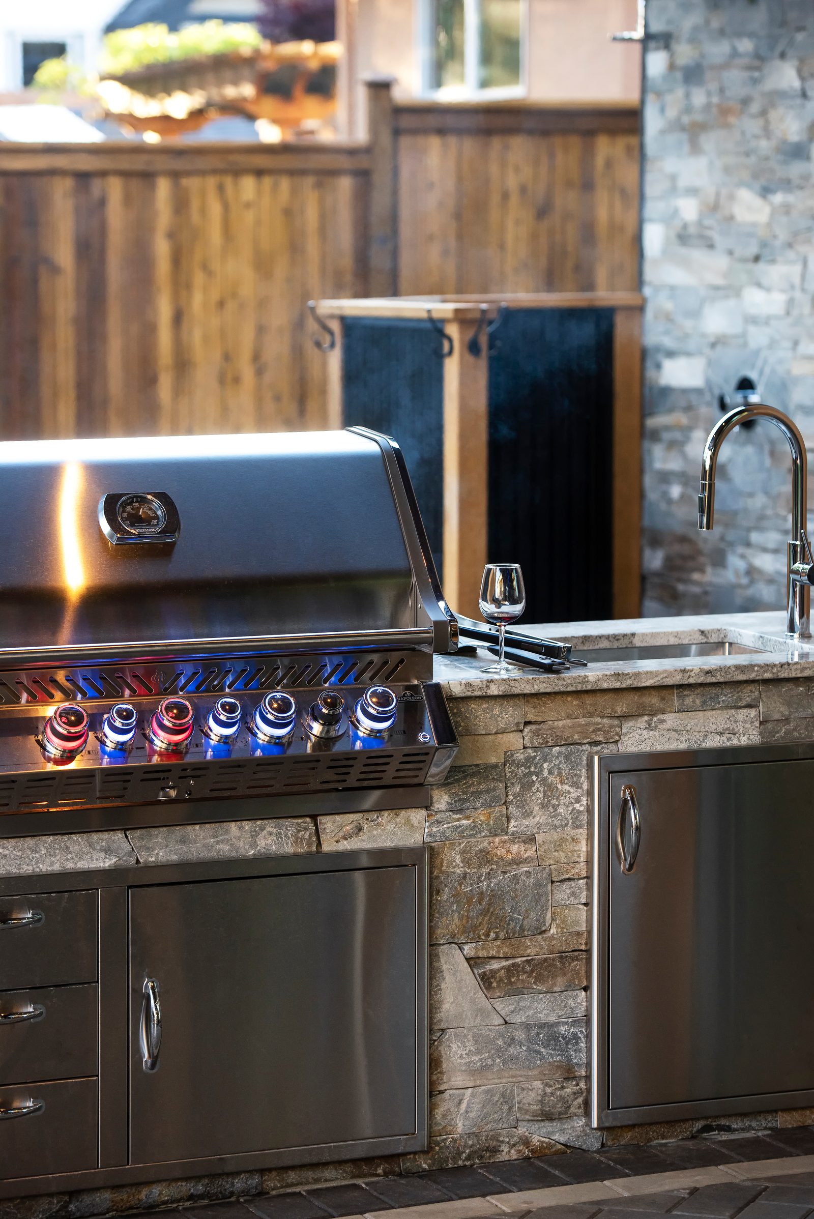 Built-in grill and sink set into a stone outdoor kitchen counter beside a cedar hot tub