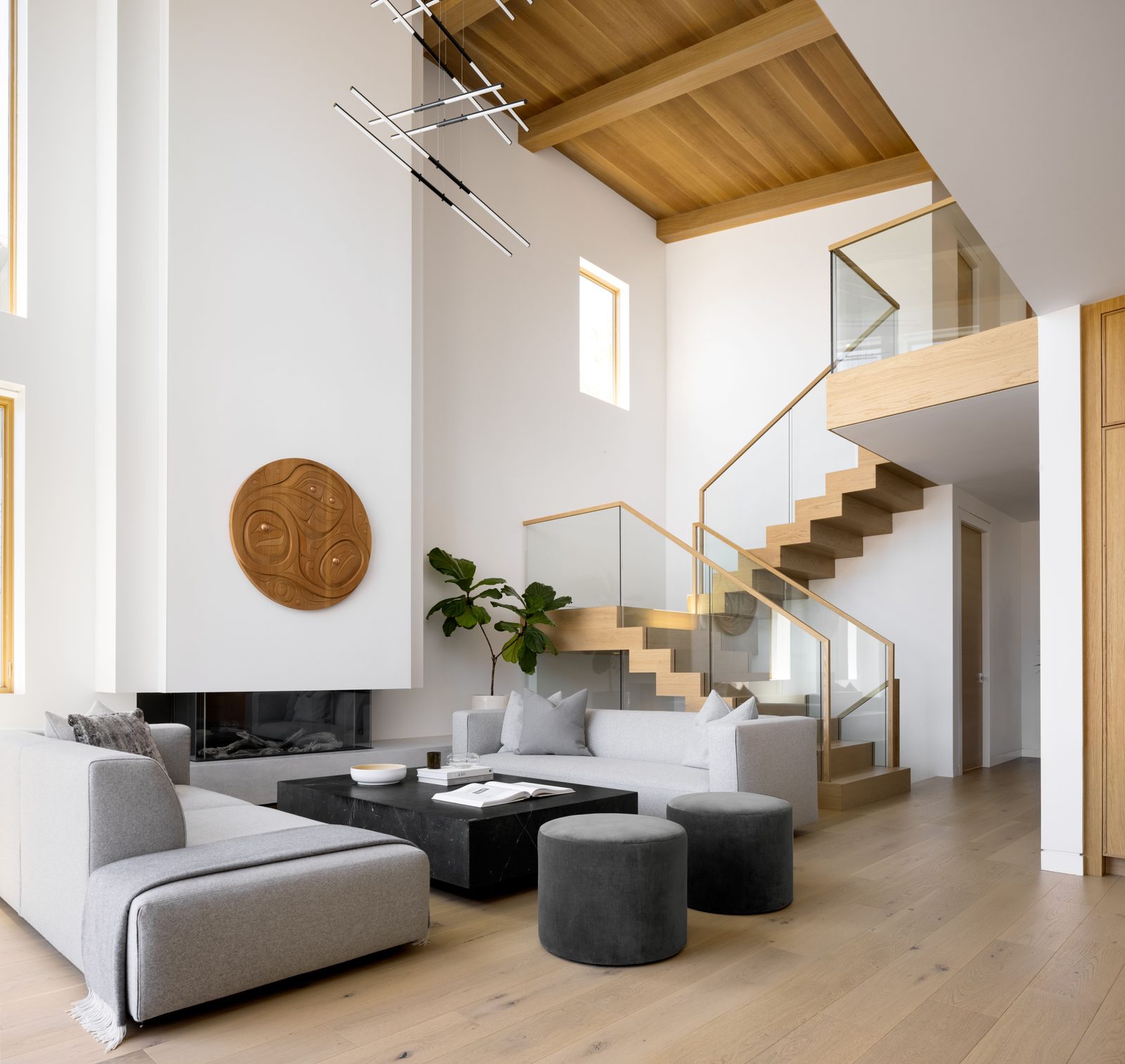 Open-tread stair rising against glass guards to a mezzanine, the beamed ceiling running out over the room below.