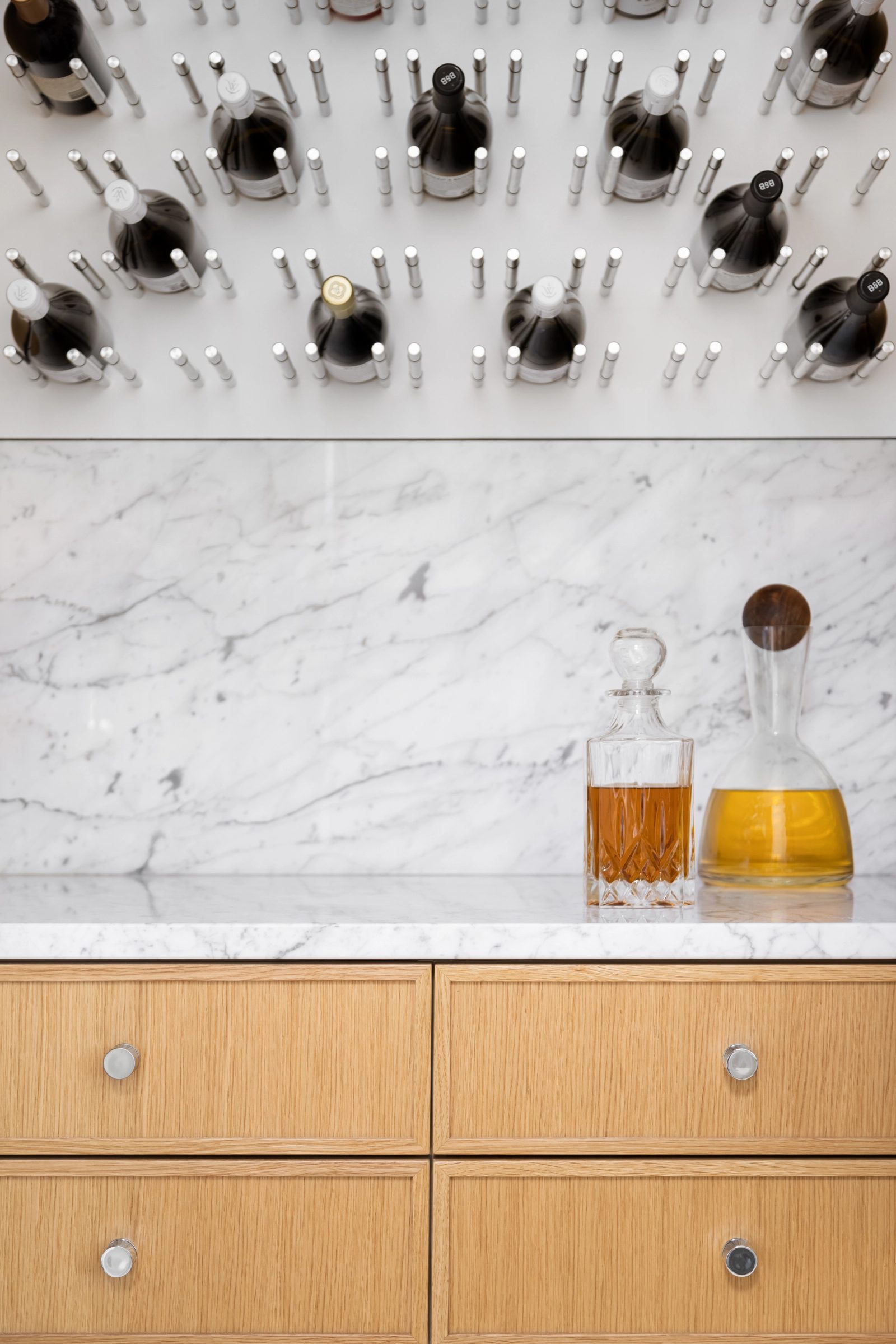 Marble counter below a wall of racked bottles, two glass decanters standing on the stone.