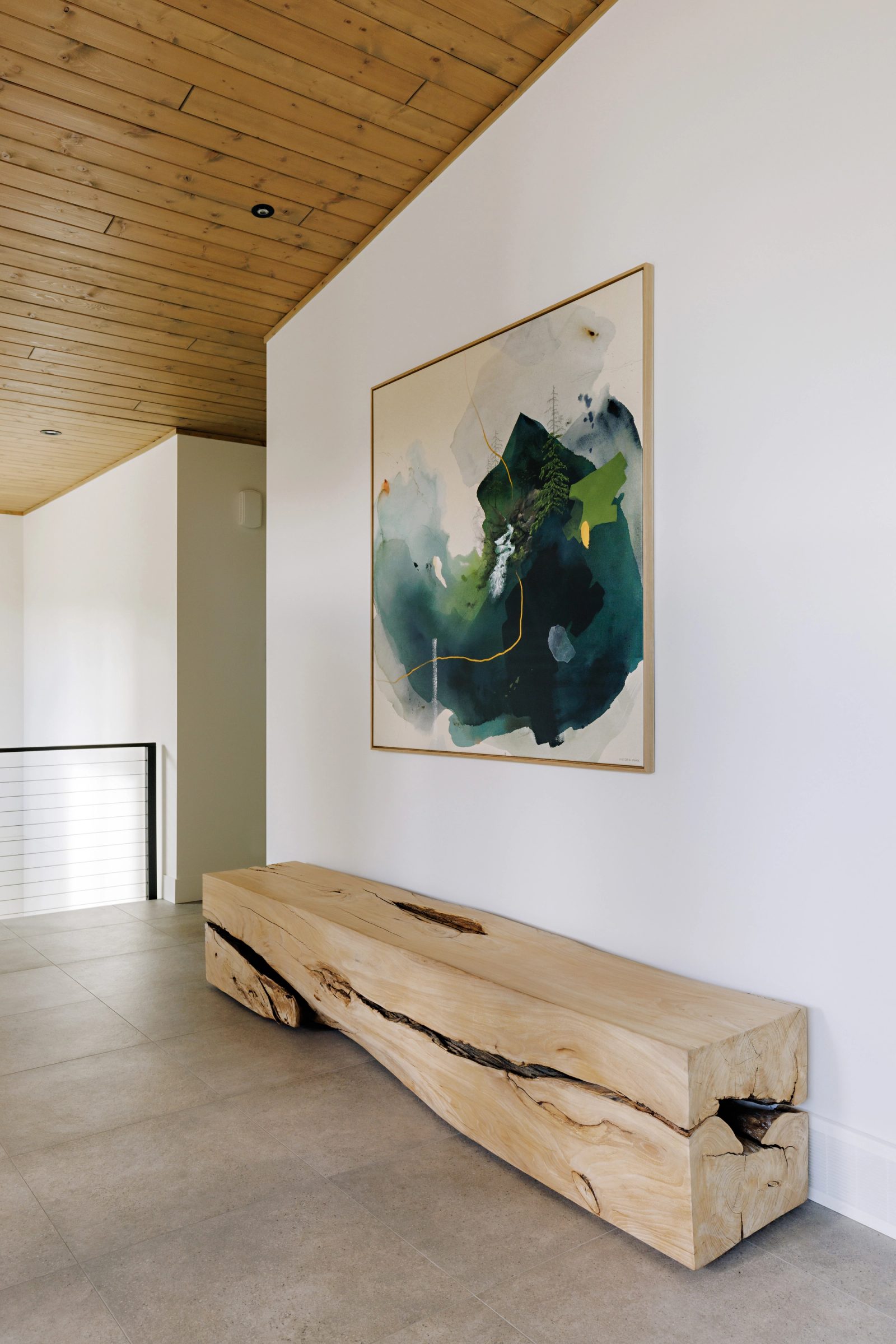 a hall opening onto a white wall hung with a large green and teal abstract canvas above a single slab of live-edge timber used as a bench.